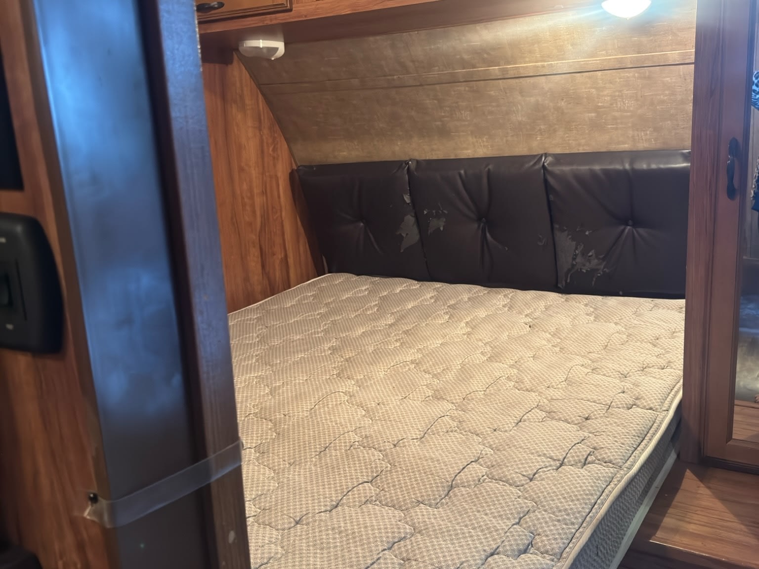RV rental bedroom view: mattress, peeling tufted headboard, wood walls, and overhead light inside.. KZ C291IKS 2015