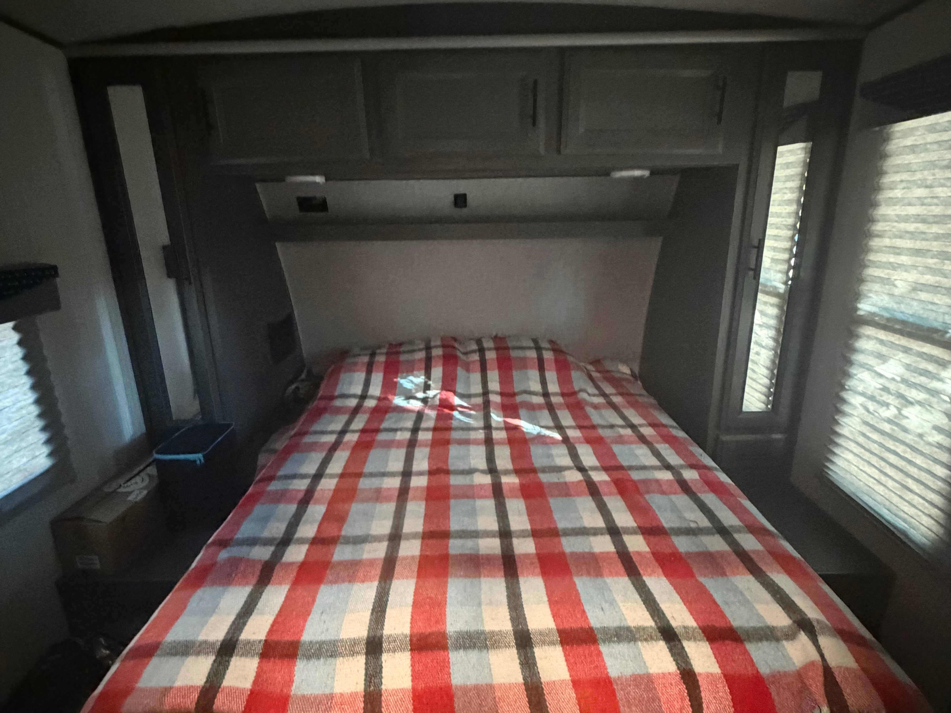 RV rental bedroom with a cozy plaid bed, overhead cabinets, and windows with blinds on either side.. Cruiser Rv Corp Stryker 2021