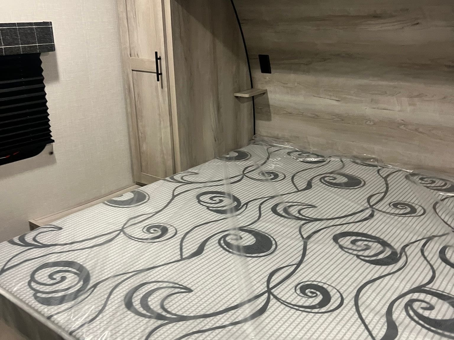 Inside a new RV rental bedroom, featuring a light-toned wood interior, wardrobe, window, and a mattress still wrapped in plastic.. Other Other 2024