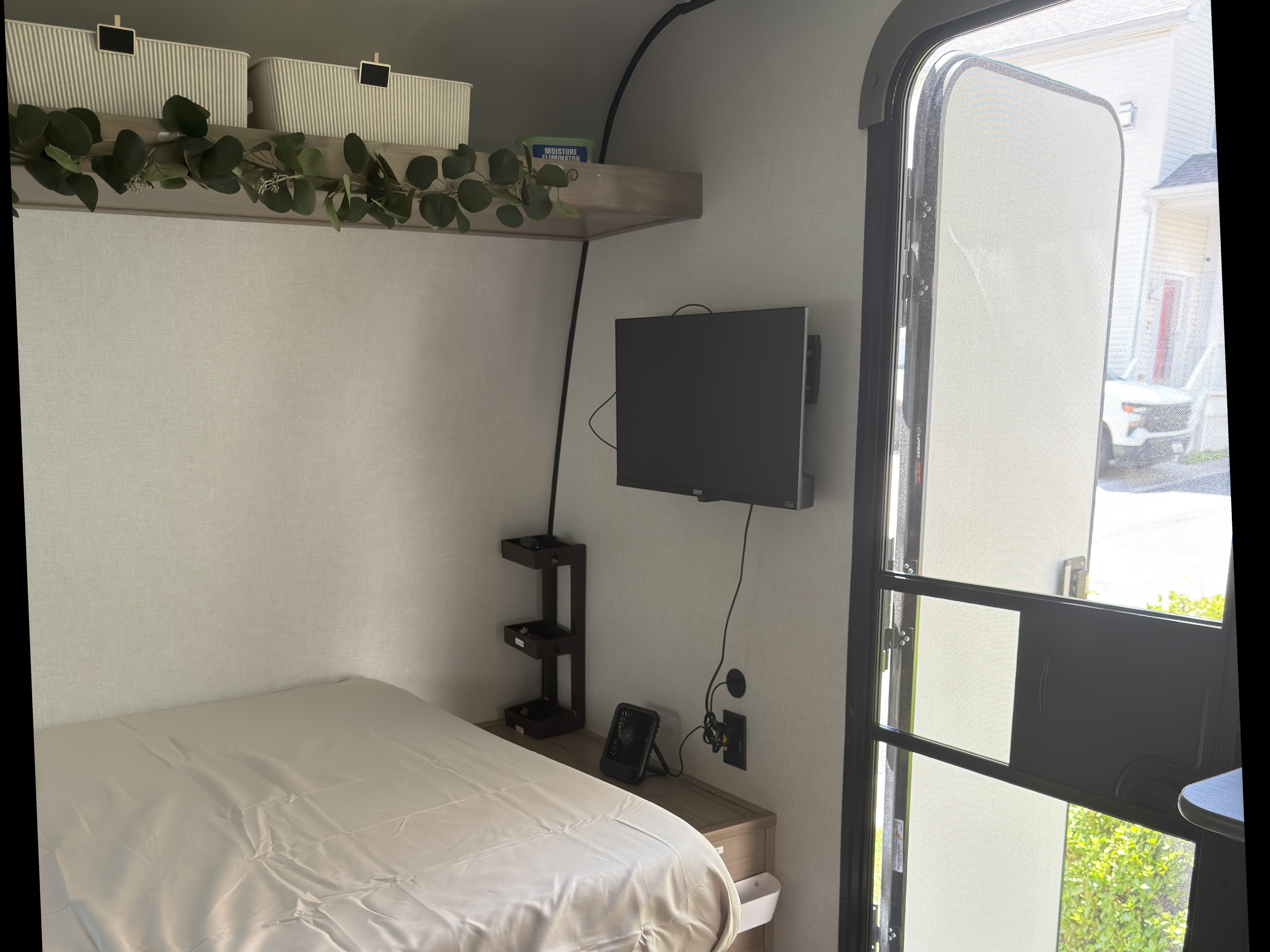 RV rental bedroom: Features a neatly made bed, wall TV, tiered storage, and a screened door offering an outside view.. Keystone RV Coleman 2026