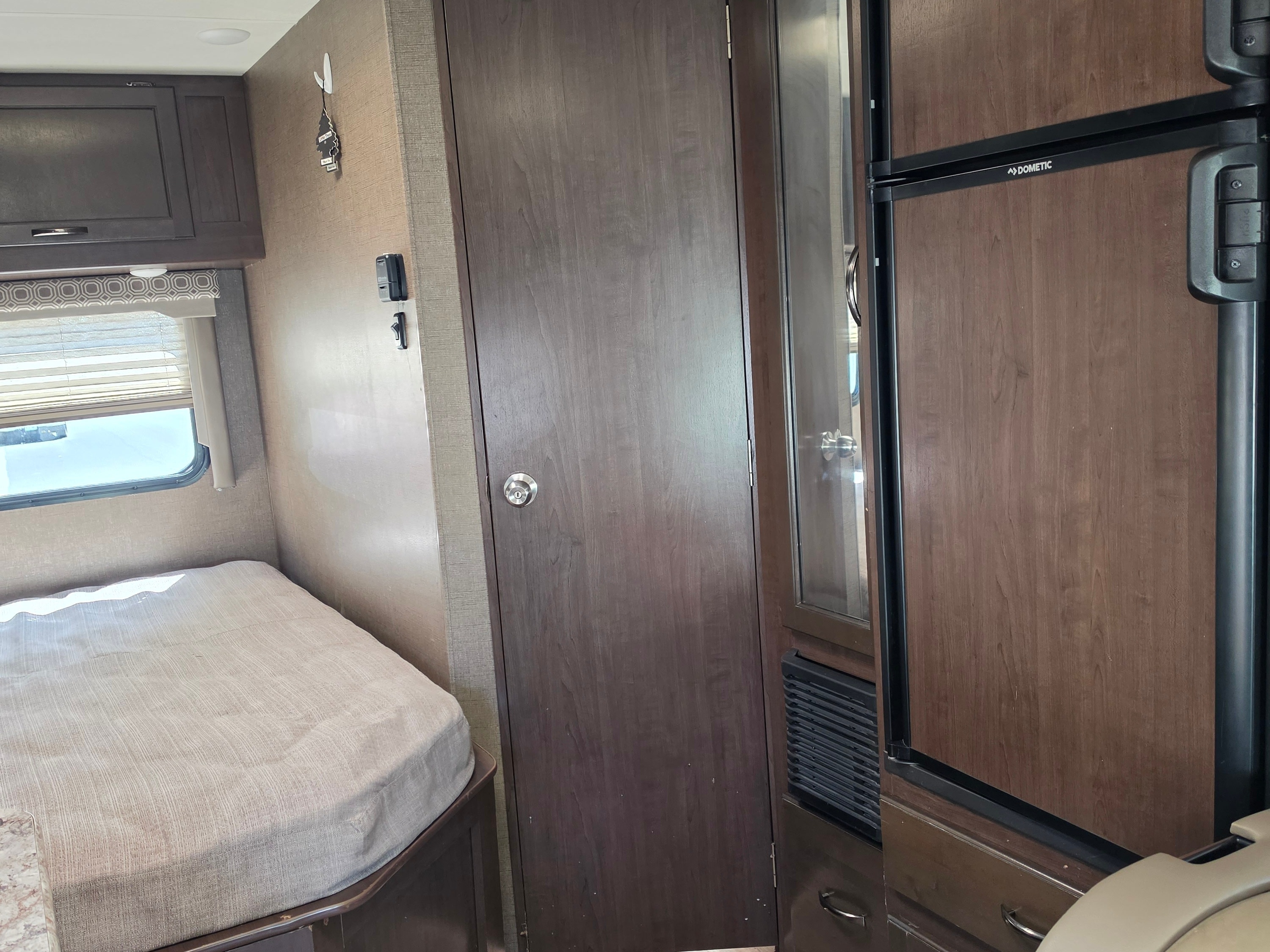 Inside an RV rental: a cozy bedroom featuring a bed, window with blinds, overhead storage, and a Dometic refrigerator.. Other Other 2020