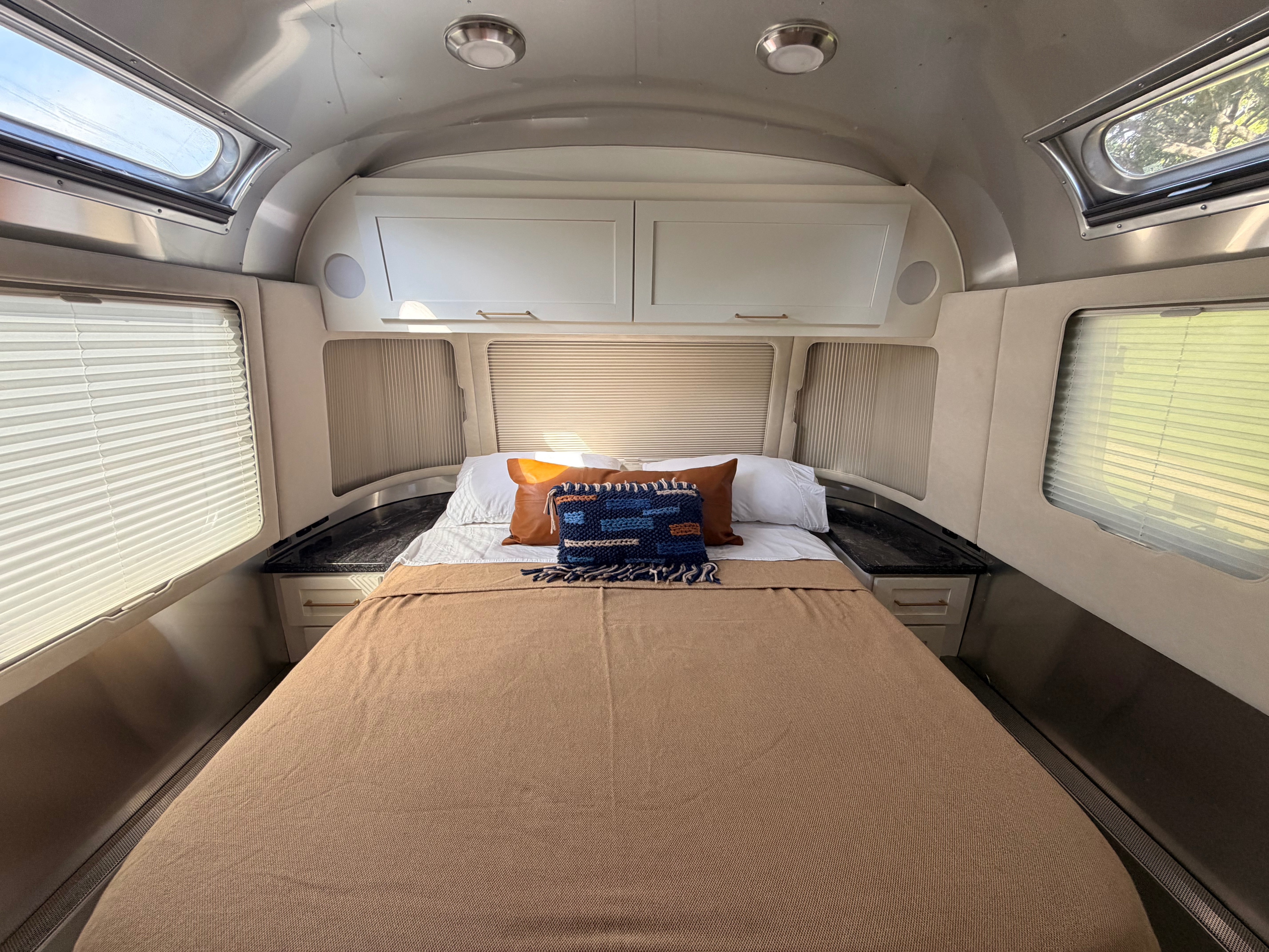 A well-appointed Airstream RV rental bedroom: bed, overhead cabinets, windows, and skylights for a bright, airy feel.. Airstream Classic 2021