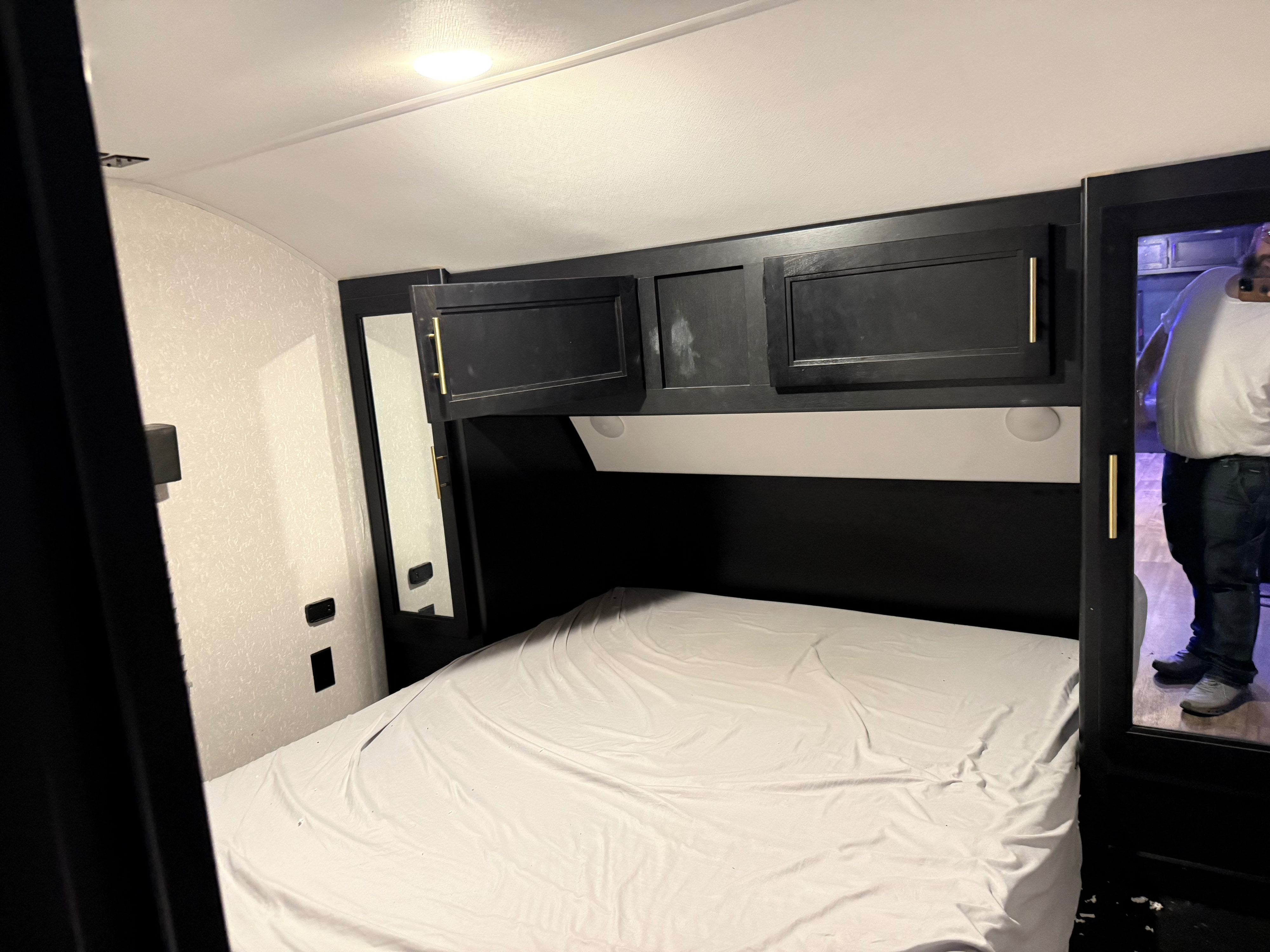RV rental bedroom: a compact space with a white bed, dark overhead cabinets, and mirrored sides. Functional design.. Forest River Cherokee 2023