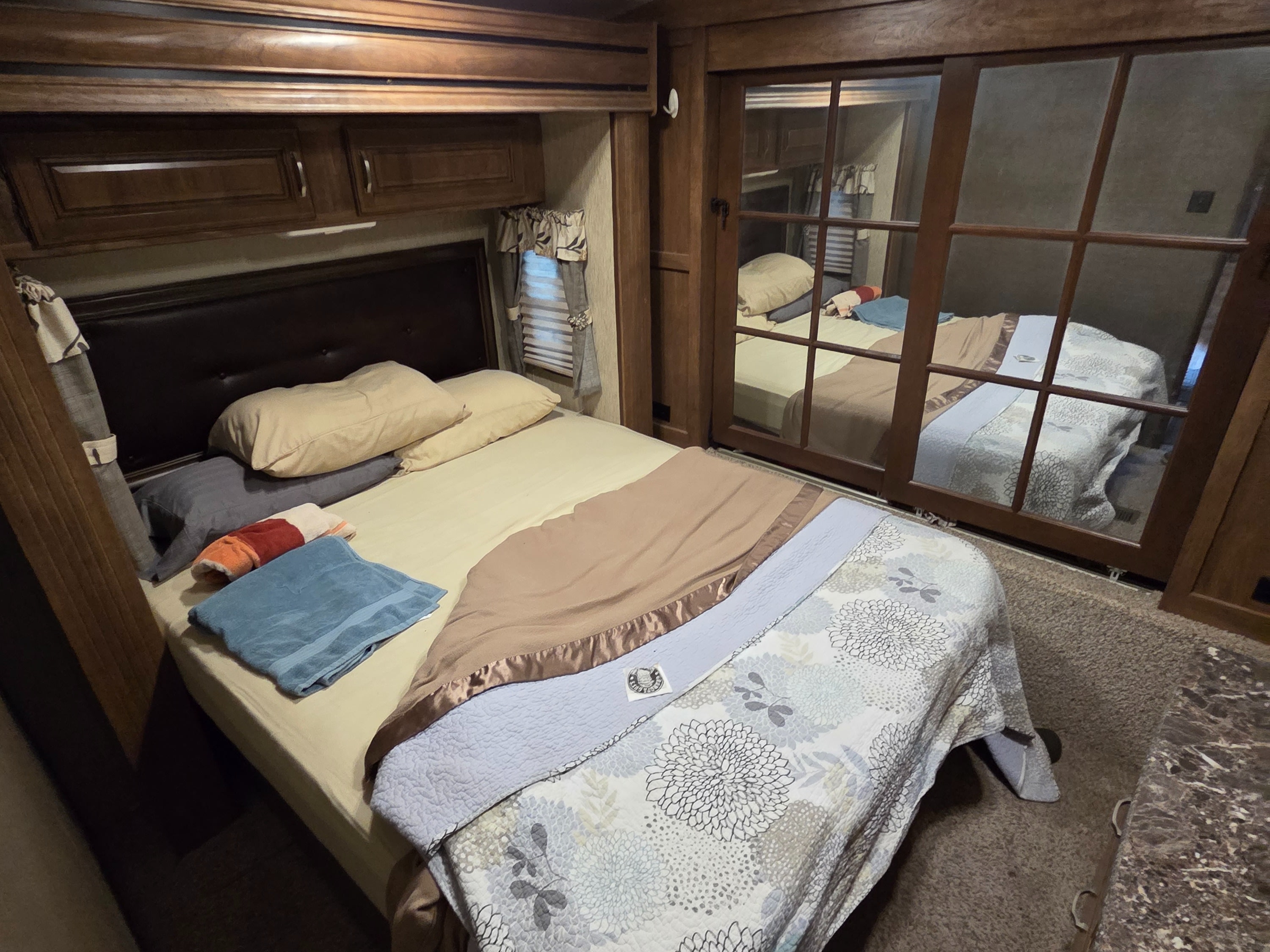 Cozy RV rental bedroom featuring a comfortable bed, overhead cabinets, a small window, and a mirrored closet.. Keystone RV Laredo 2016