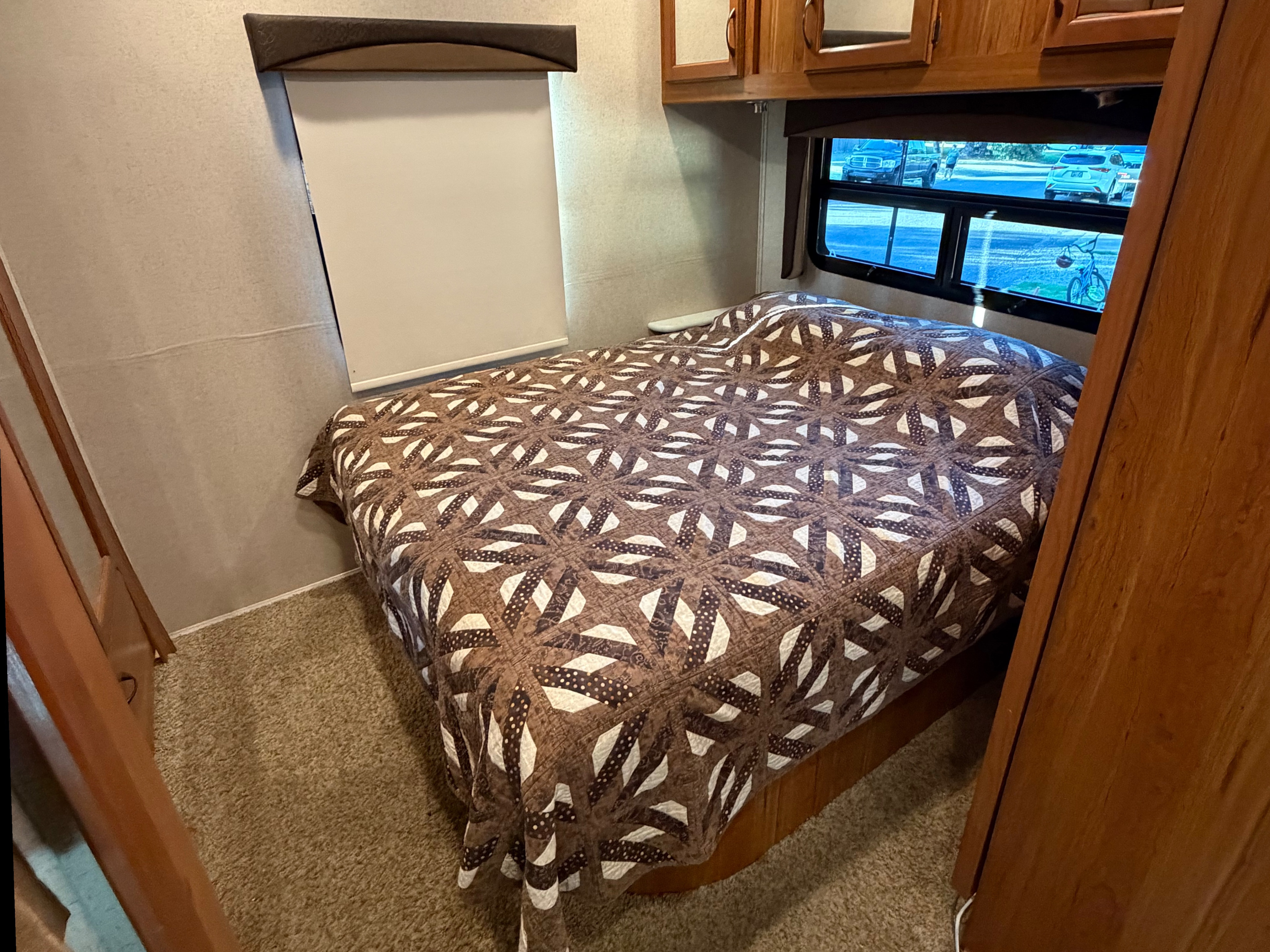 Cozy RV rental bedroom interior with a patterned quilt on the bed, window view, and wooden cabinetry.. Jayco Greyhawk 2016