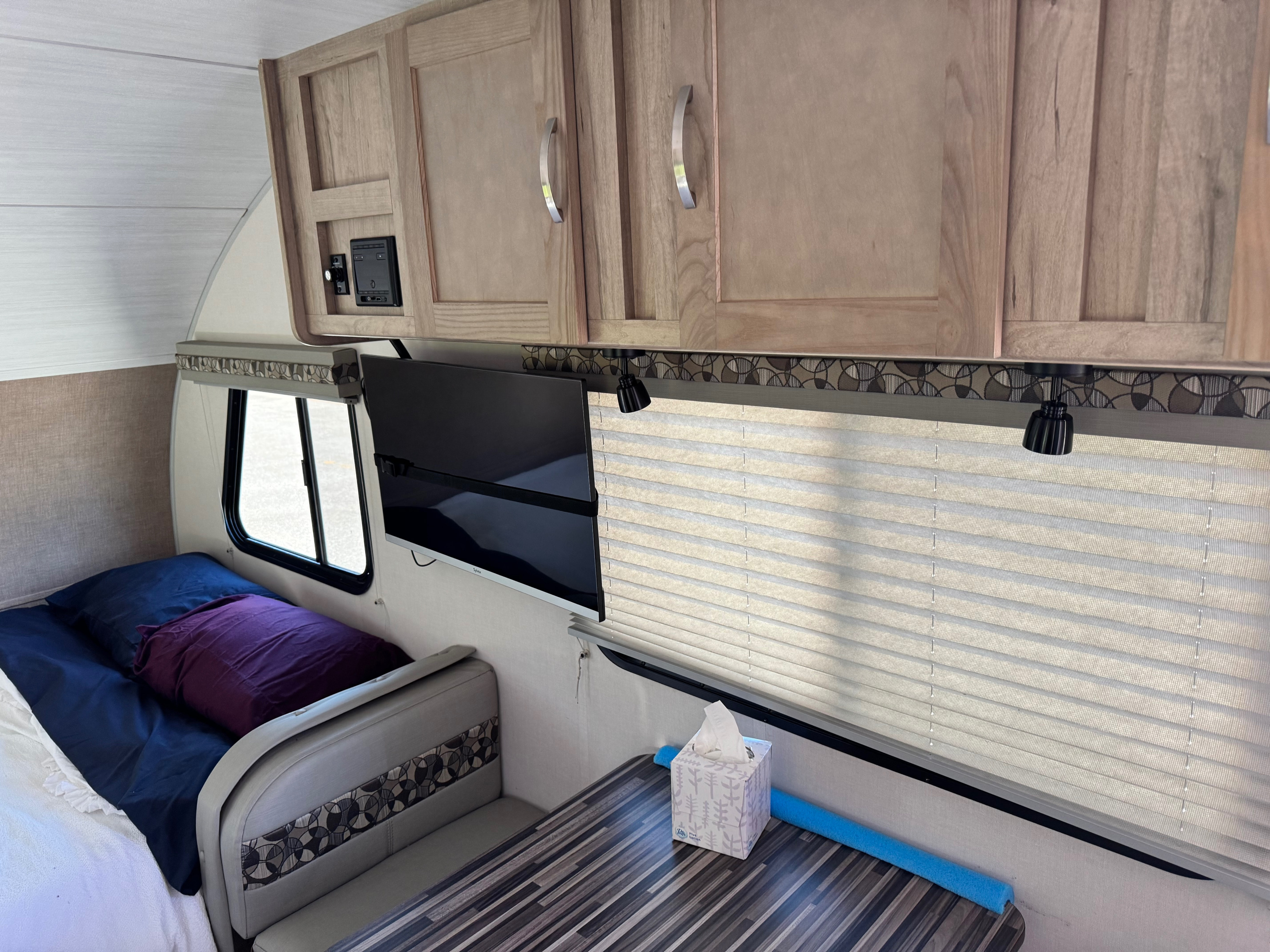 Inside an RV rental: a compact interior featuring a bed, mounted TV, dining area, and wooden overhead cabinets.. R-Pod R-Pod Trailer 2020
