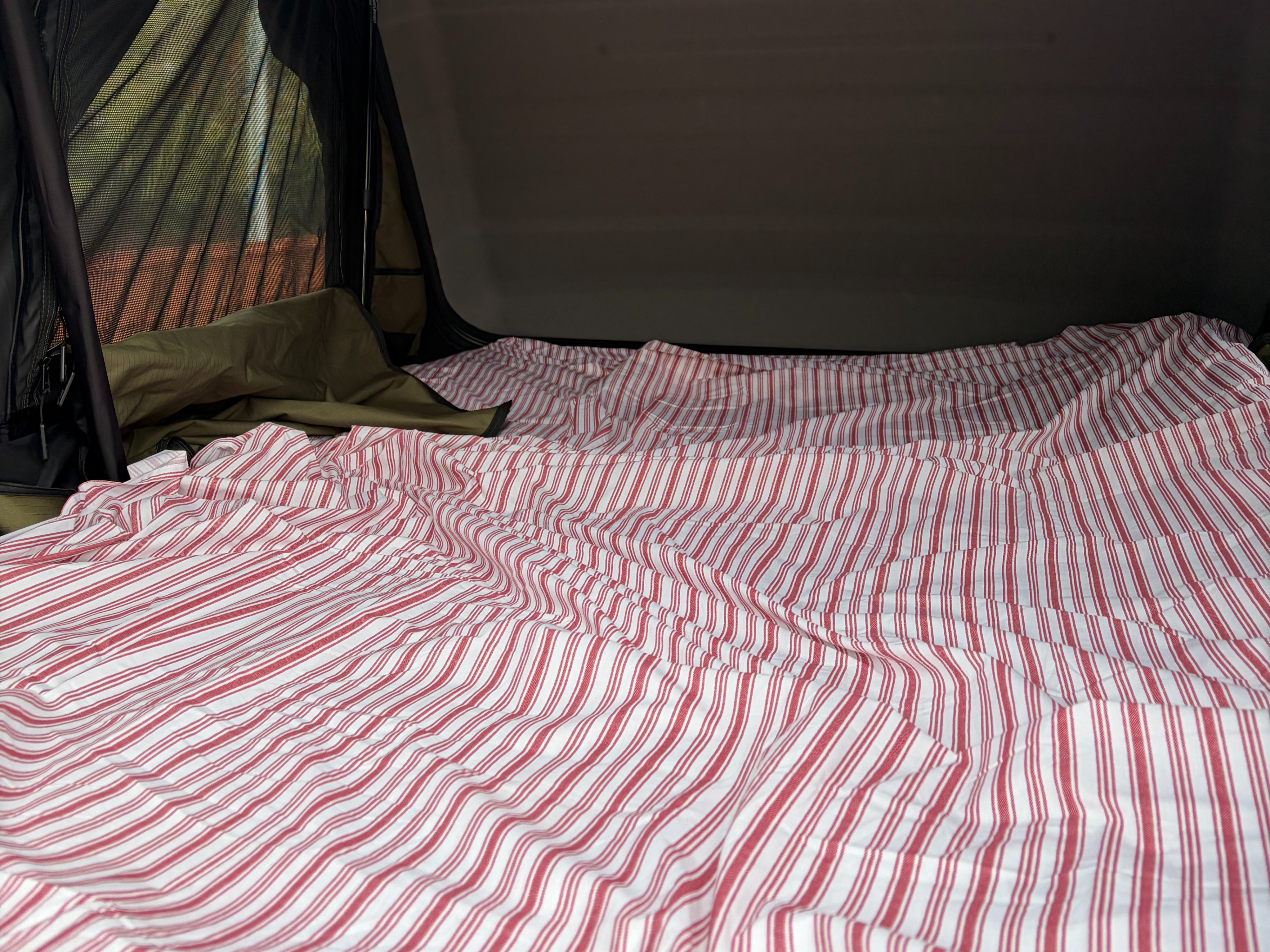Comfortable striped bed in an RV rental's sleeping area with a mesh window view, perfect for camping.. Ford Bronco 2021