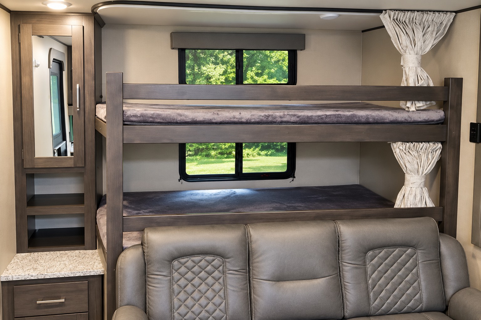 This RV rental interior offers bunk beds, a comfortable sofa, and cabinet storage. Windows show green trees, ideal for family trips.. Grand Design Transcend Xplor 2022