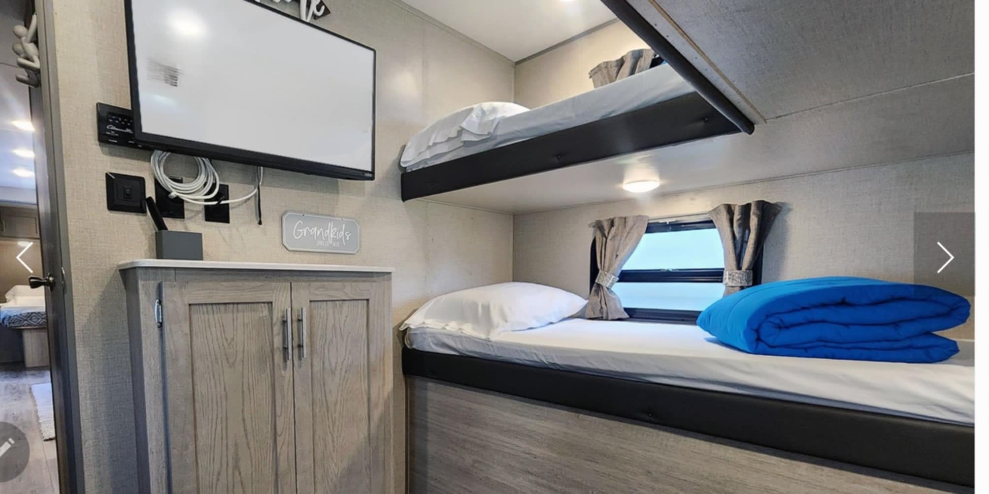 RV rental interior: cozy bunk beds with pillows, blankets, a TV, and storage cabinet. Ideal for family adventures.. Coachman Catalina 2022