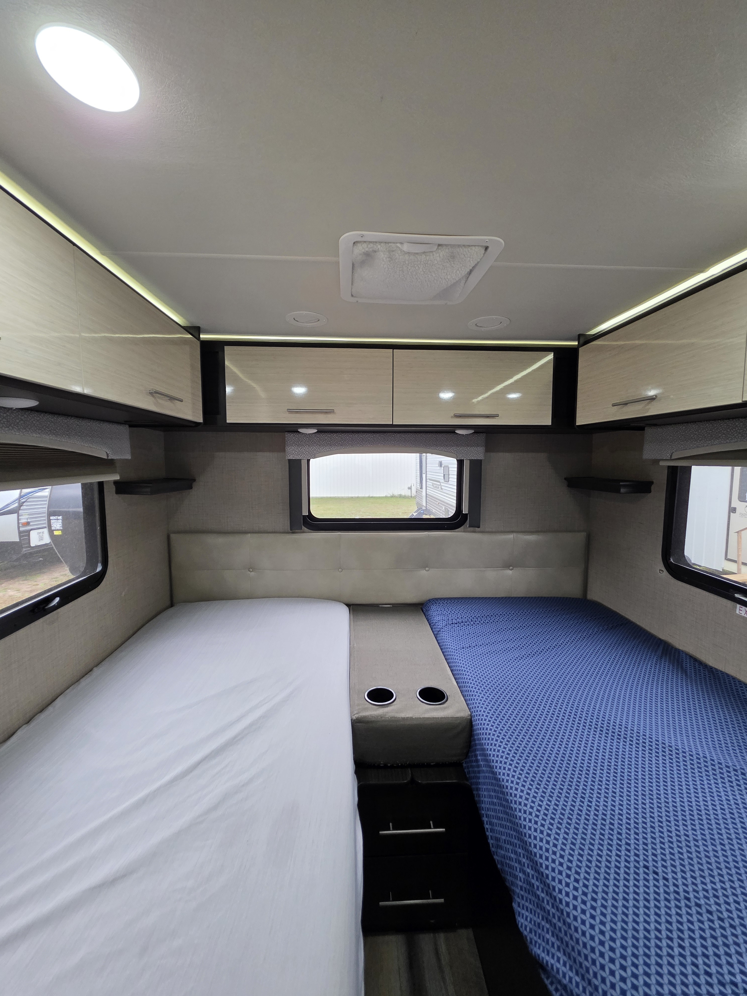 Cozy RV rental bedroom with two beds, overhead storage, and cup holders, perfect for a comfortable trip.. Thor Vegas 2019