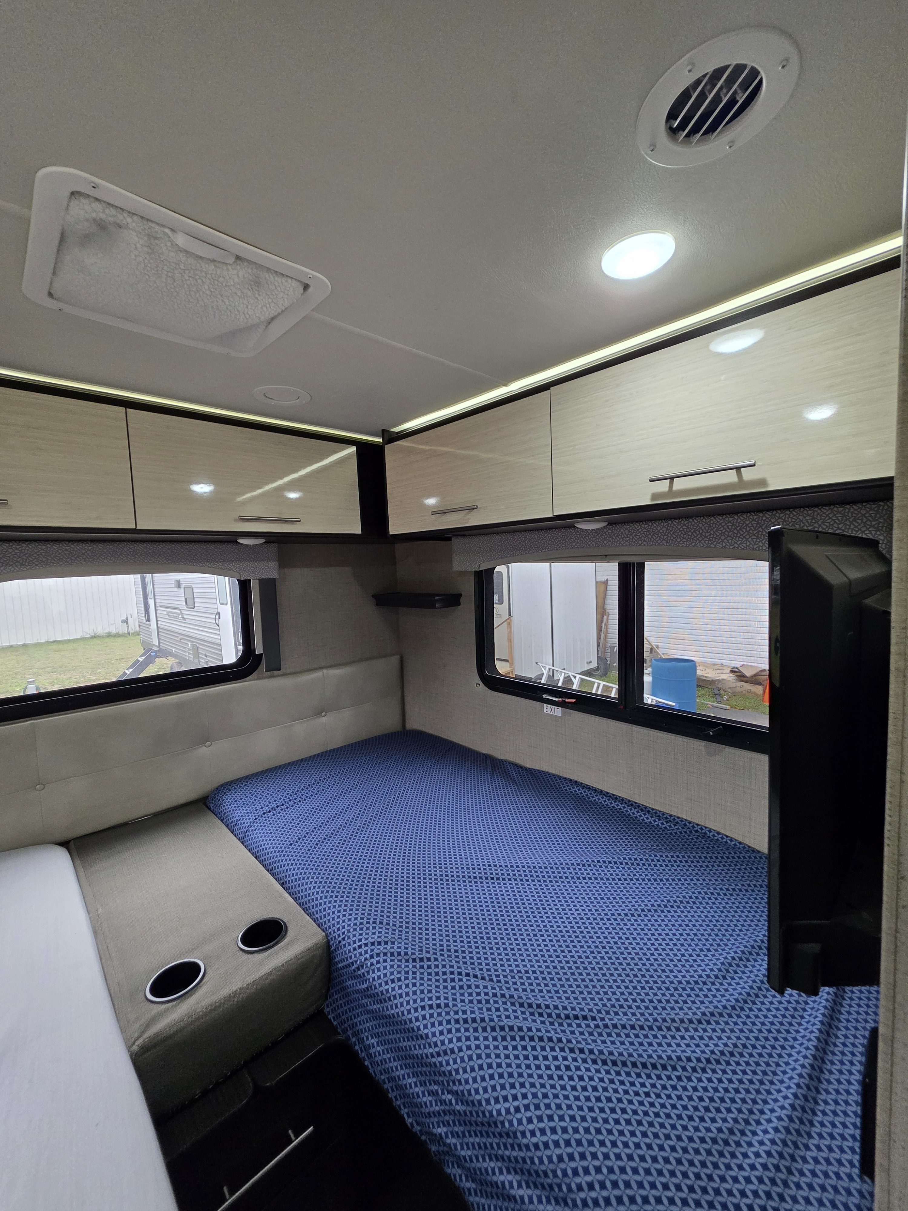 Cozy rv rental bedroom area with blue patterned bed, windows, overhead cabinets, and built-in cup holders.. Thor Vegas 2019