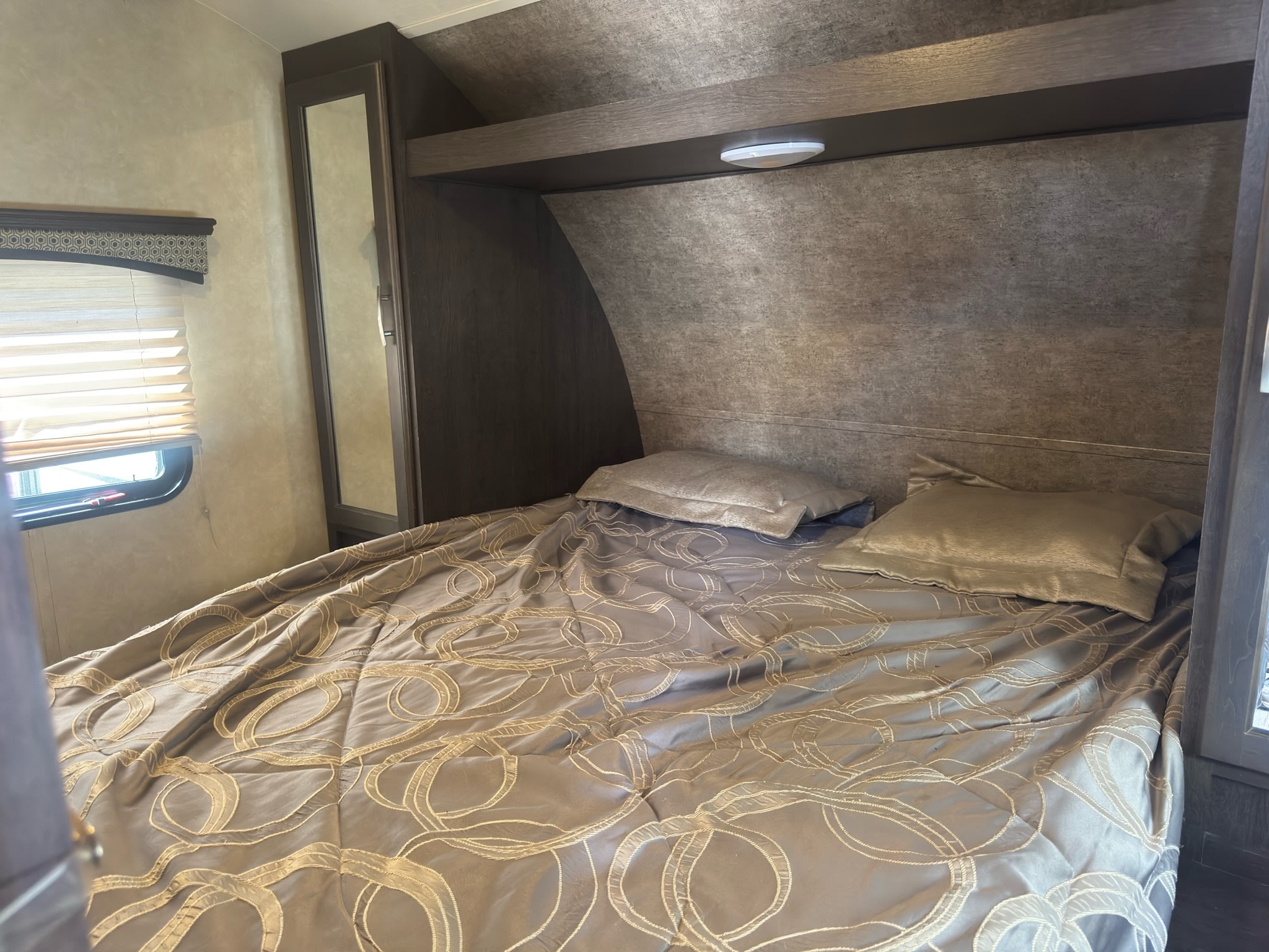 Step into a comfortable RV rental bedroom, featuring a patterned comforter on the bed, overhead shelf, and window blinds.. Forest River 270BHS 2016