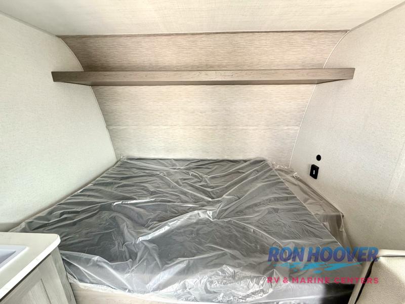 RV rental's clean sleeping area: new bed, overhead shelf & outlet. Bright interior for comfortable camper trips.. Hideout Sport 140RE 2025