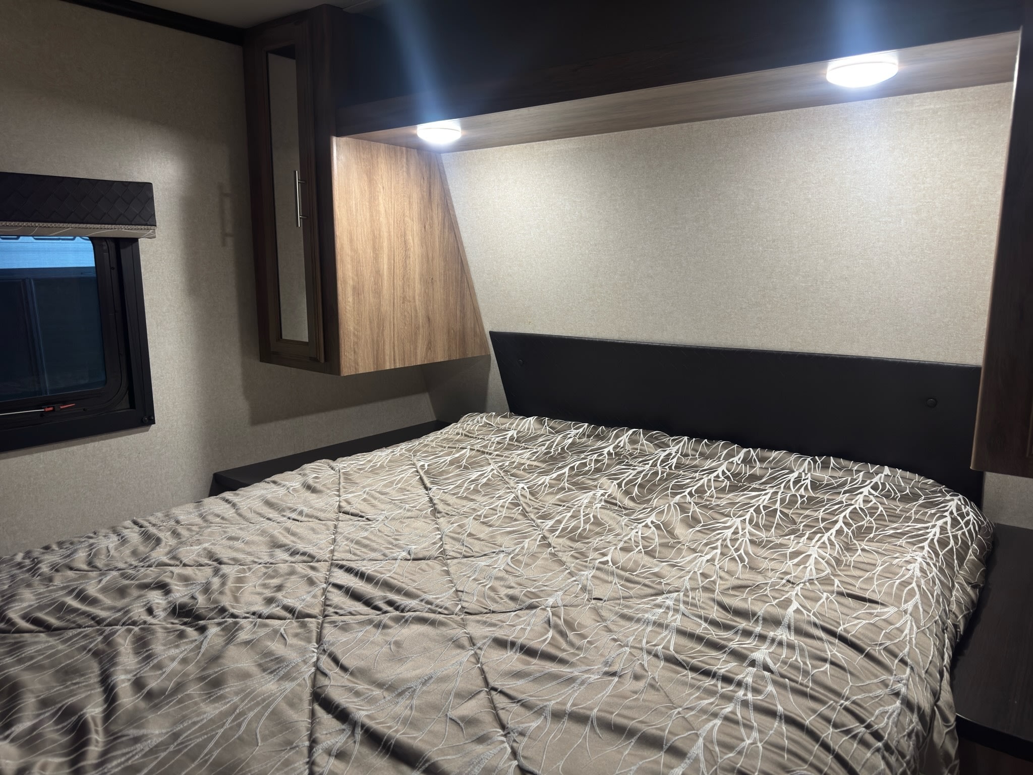 Cozy rv rental bedroom showing a bed with a unique comforter, overhead storage, and bright reading lights.. Jayco Jay Feather 2018