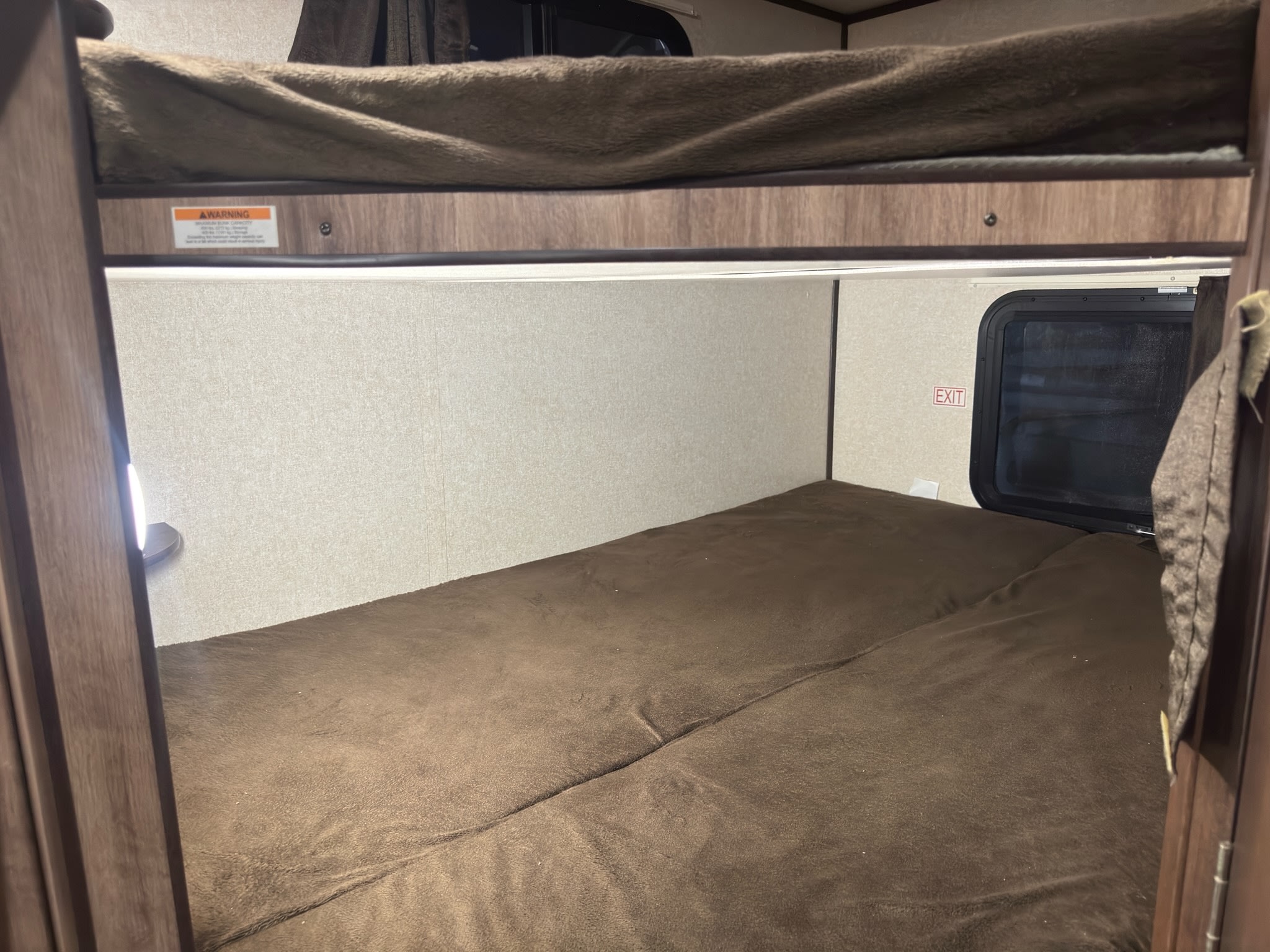 Cozy RV rental bunk beds, a sleeping area inside a camper with a visible warning label and exit sign.. Jayco Jay Feather 2018