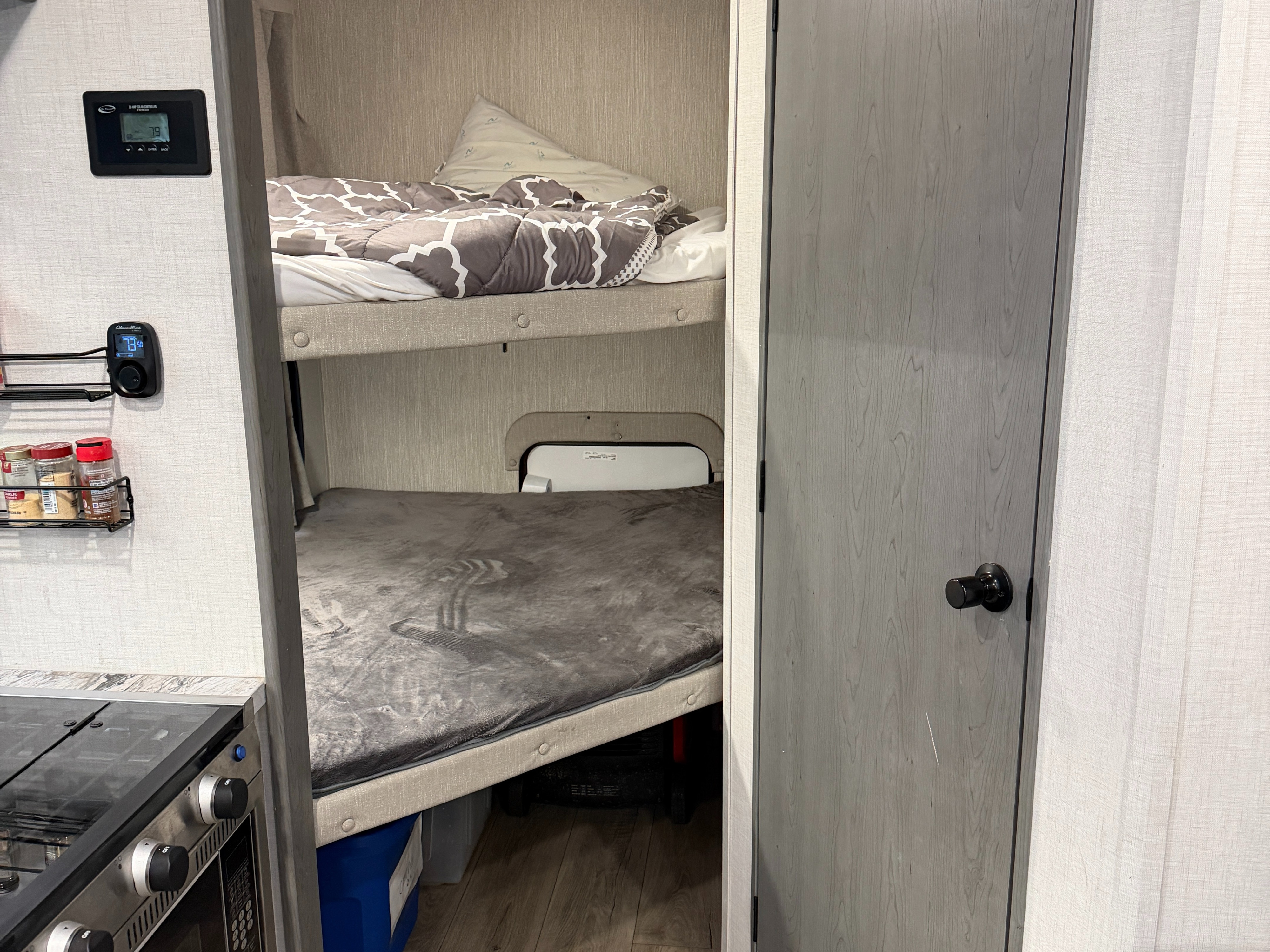RV rental interior showcasing bunk beds with bedding, a kitchen stove, spice rack, and climate controls.. Forest River 2690BHK Ozark 2025