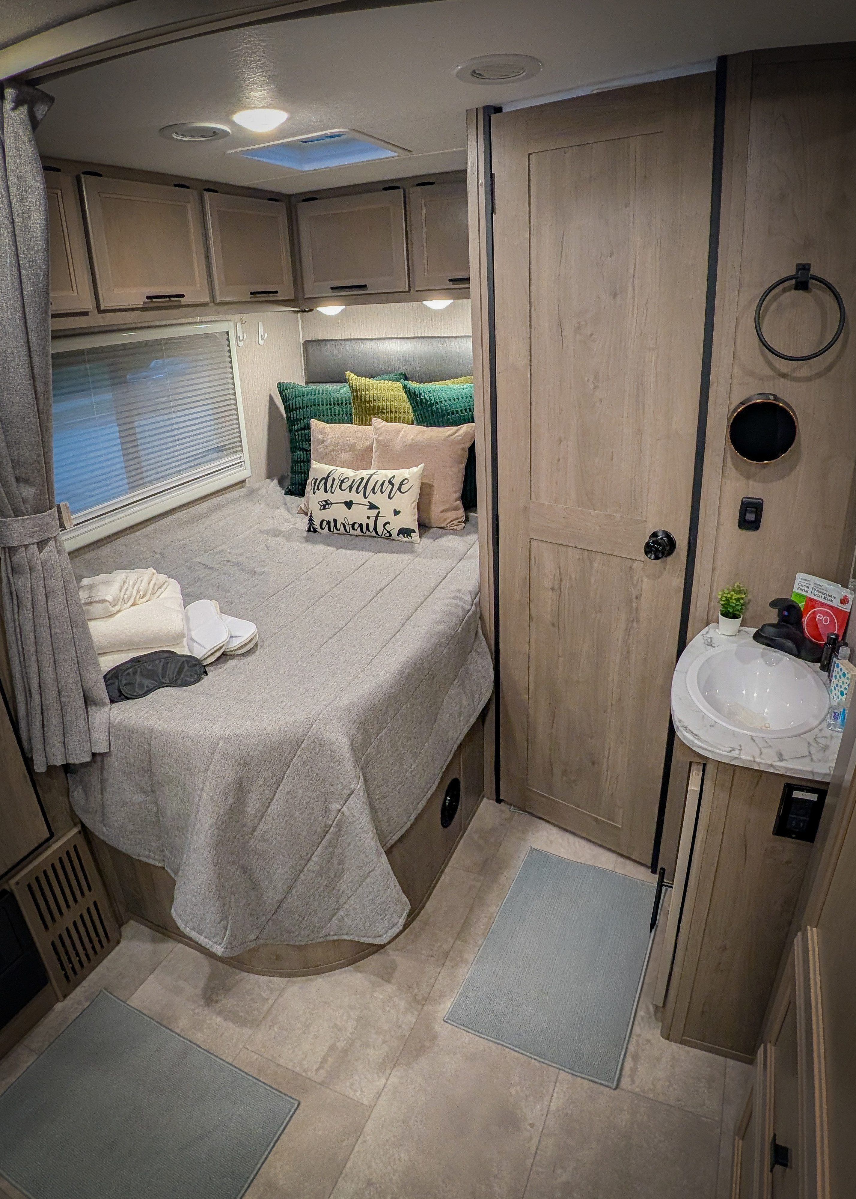 Cozy RV rental interior featuring a neatly made bed with "adventure awaits" pillow, overhead storage, and a compact sink area.. Coachmen Prism 2022