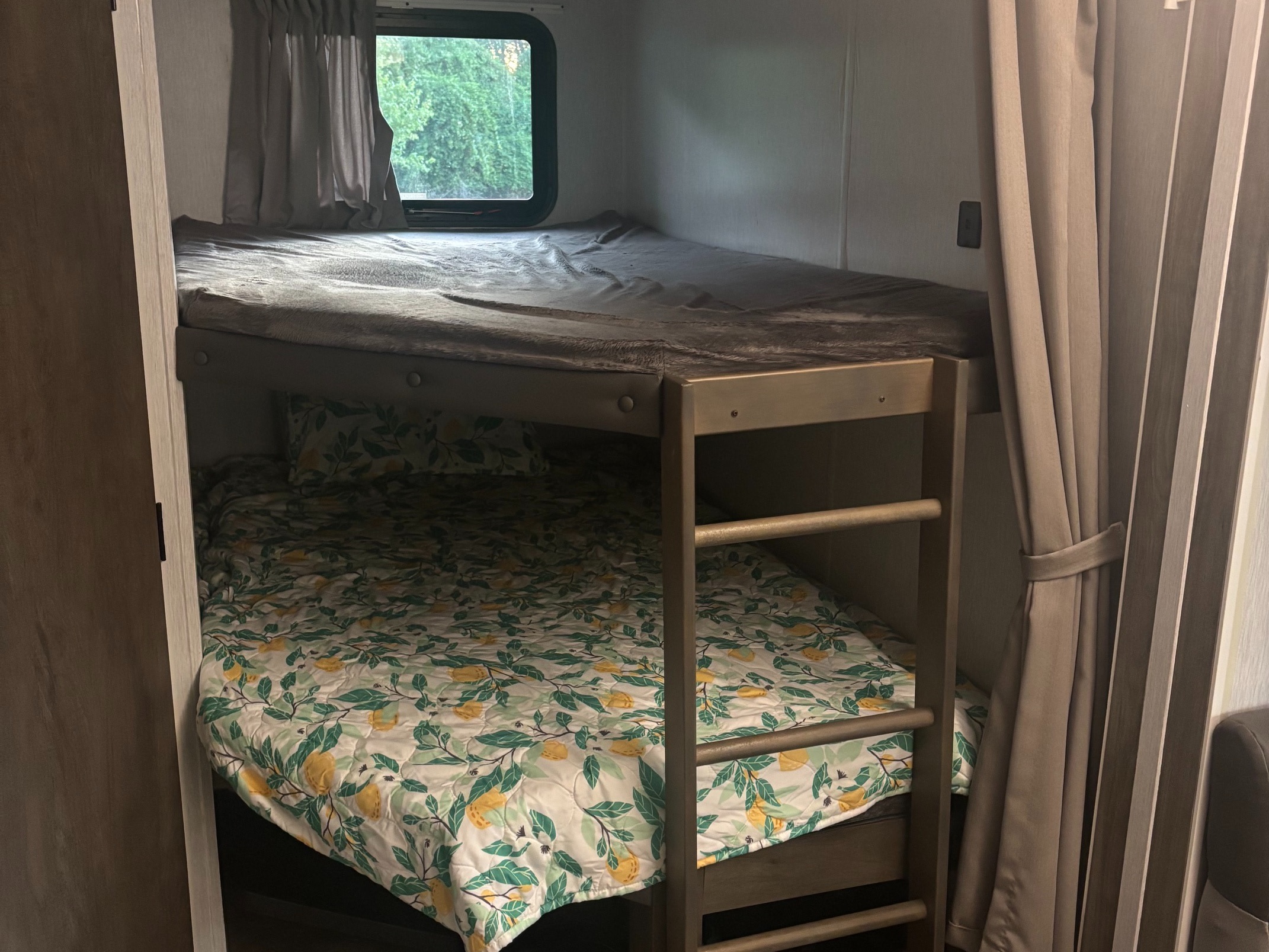 Relax in your rv rental: a cozy bunk bed setup with a grey blanket on top and a lemon-print quilt below, by a window.. Forest River Salem 2022