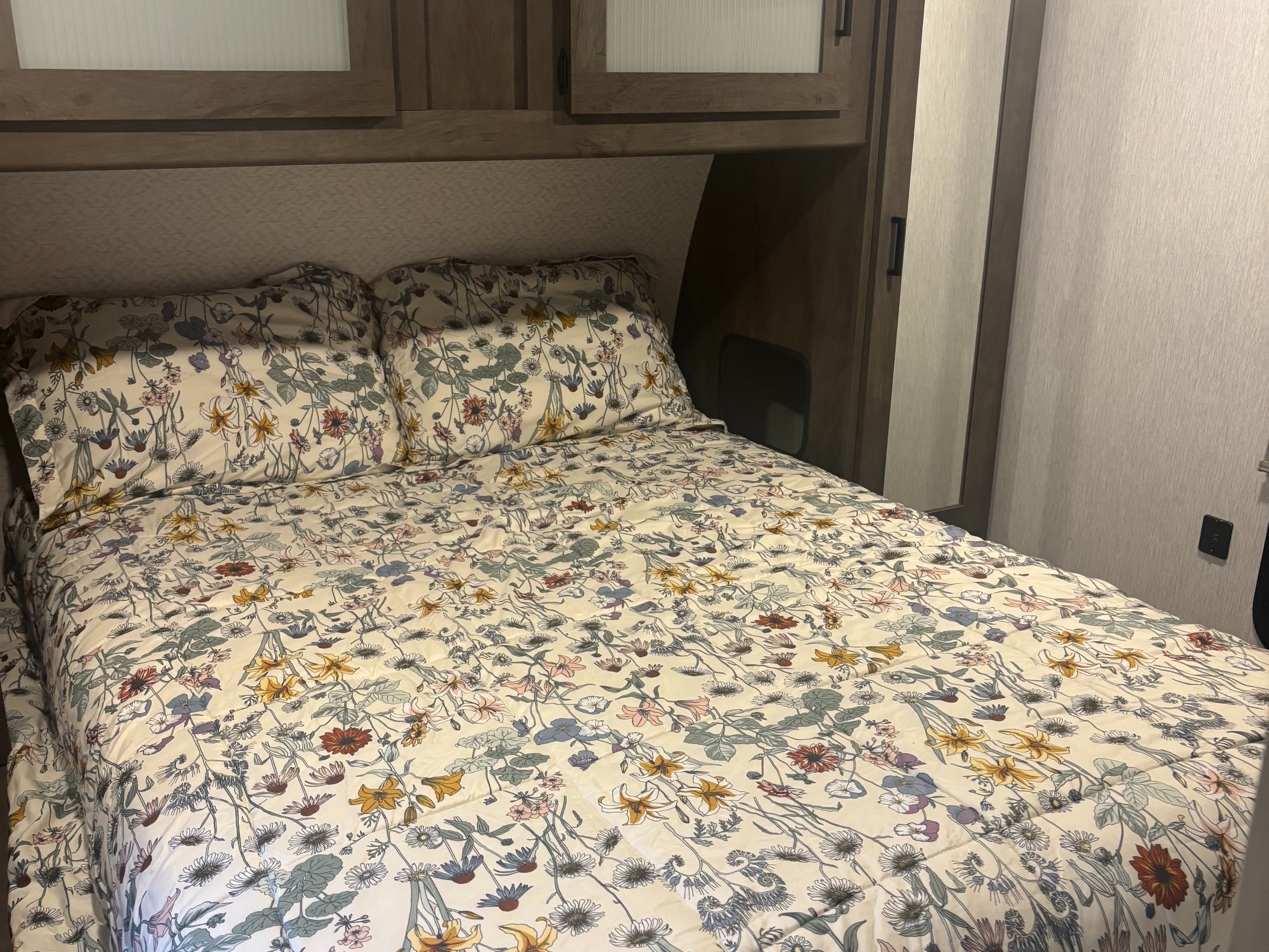 A cozy bed with vibrant floral bedding fills a compact rv rental bedroom, featuring overhead wooden cabinets.. Forest River Salem 2022