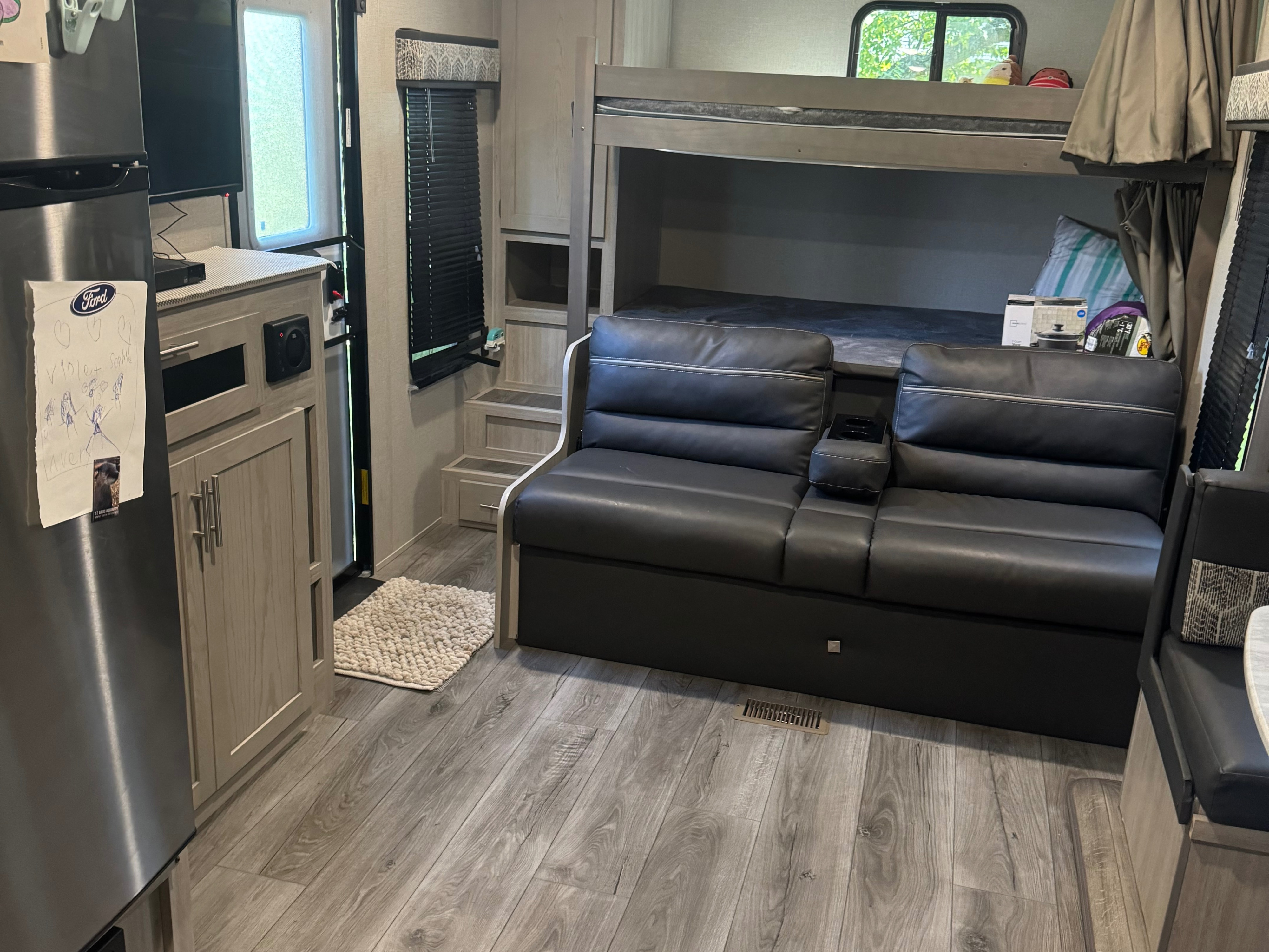 Cozy RV rental interior: Bunk beds, black leather sofa, fridge, light wood cabinets, and wood-look floor.. Coachmen Catalina summit series 8 2023