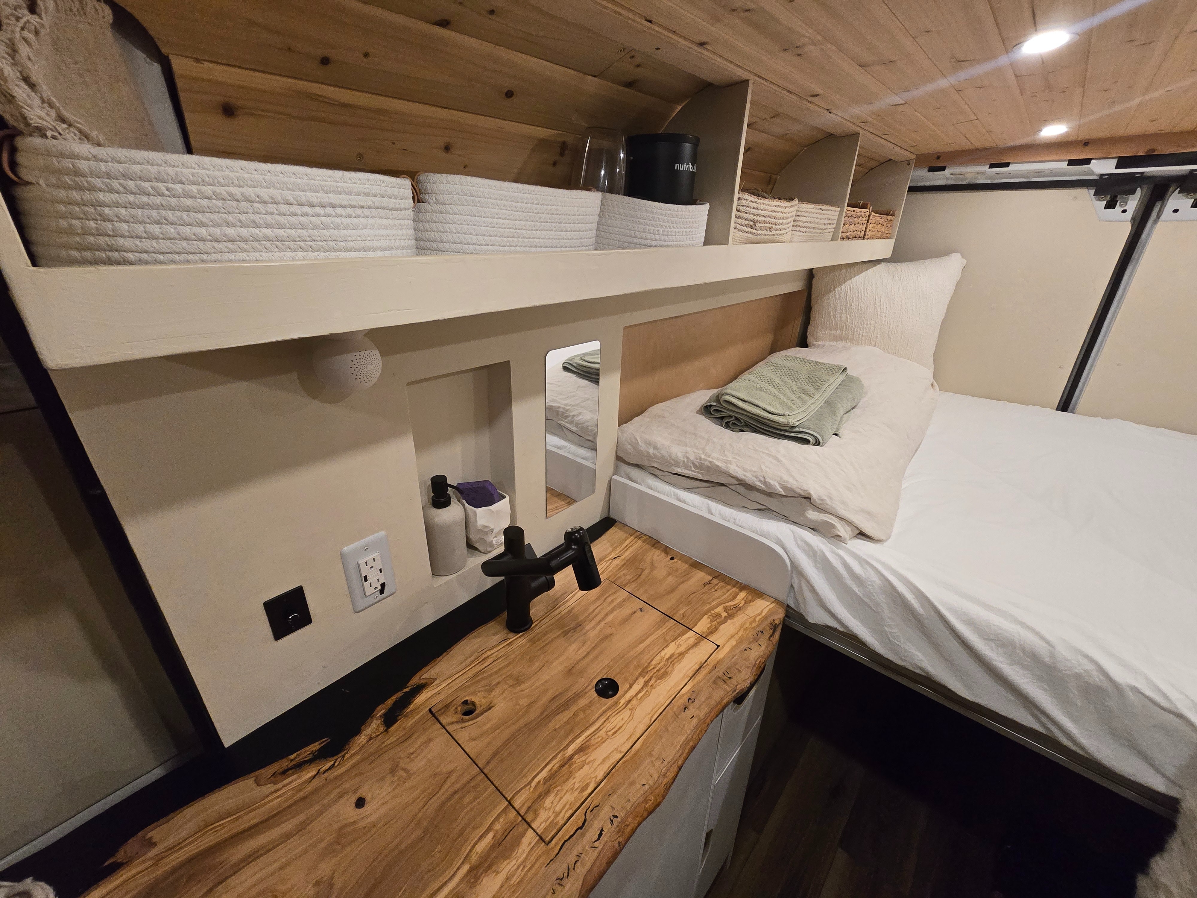 Modern rv rental interior: a comfy bed, live-edge counter with sink, and smart storage shelves. Ideal for compact living.. Dodge 1500 2023