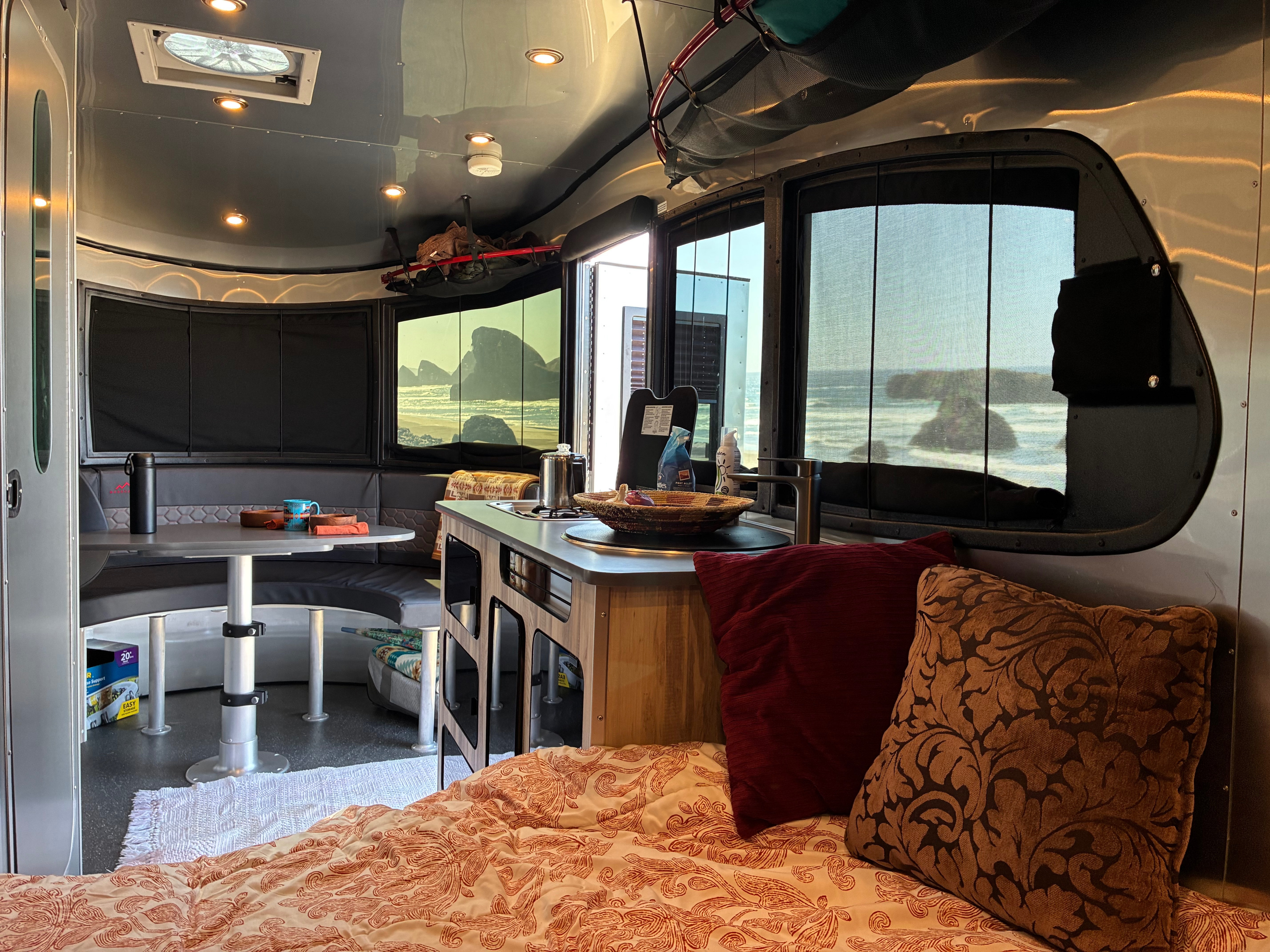 Cozy RV rental interior with an ocean view, featuring a bed, kitchenette, and dinette for a comfortable trip.. Airstream Basecamp 2023