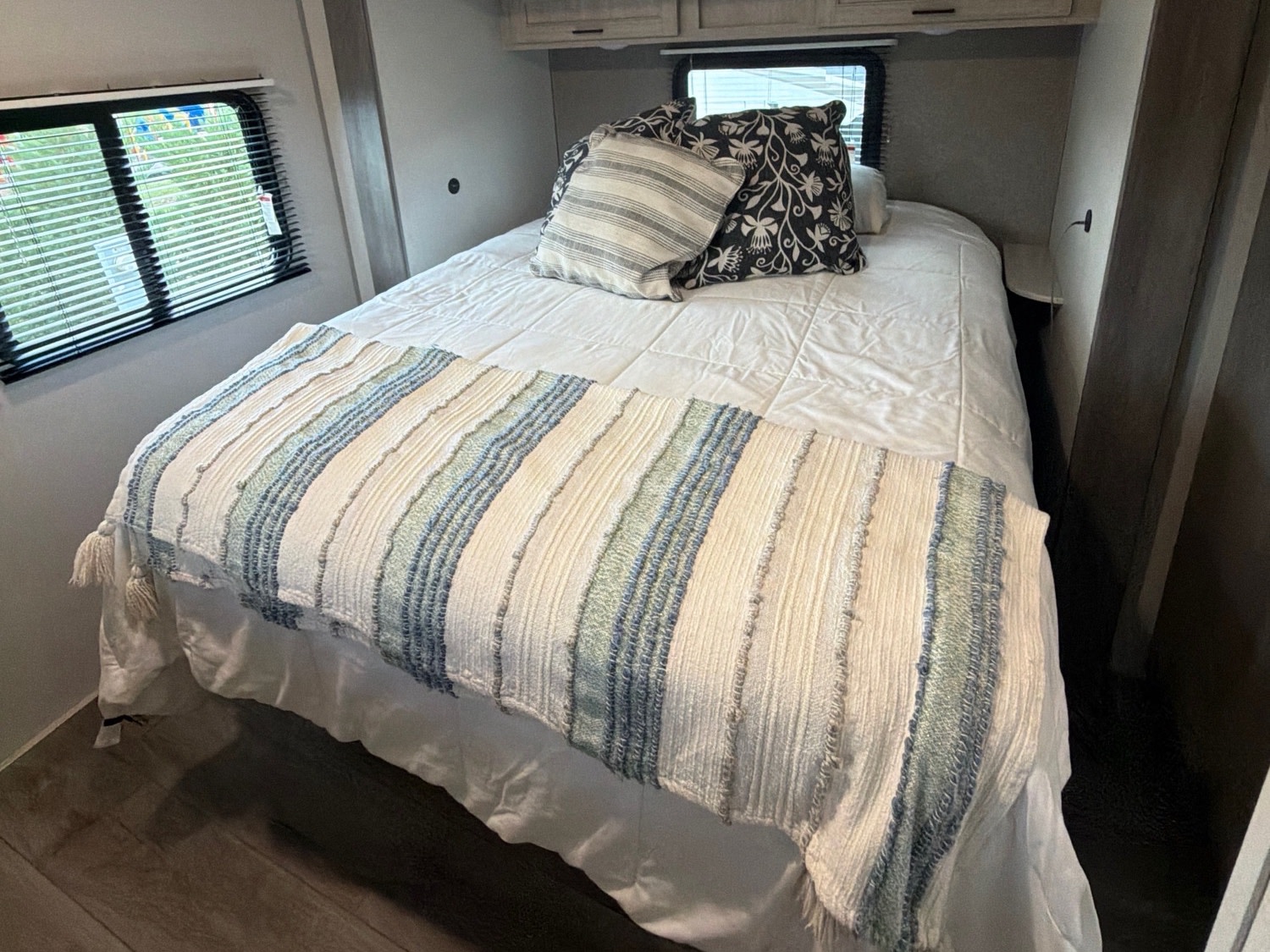 Comfortable RV rental bedroom featuring a striped blanket, soft pillows, and a window with blinds.. Coachmen Catalina Legacy 2024