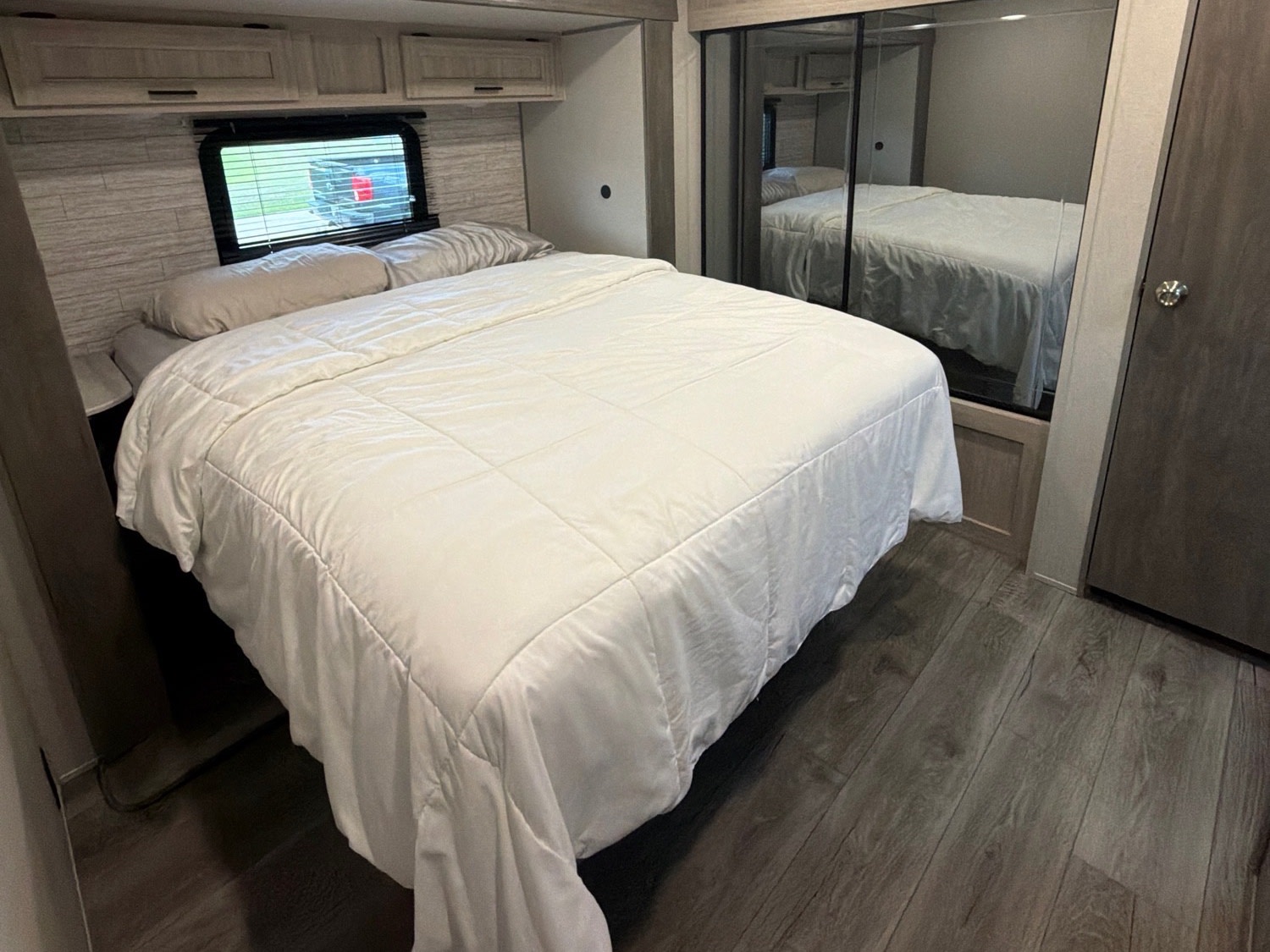 This RV rental bedroom features a comfy bed, mirrored closet, overhead storage, and a window for natural light.. Coachmen Catalina Legacy 2024