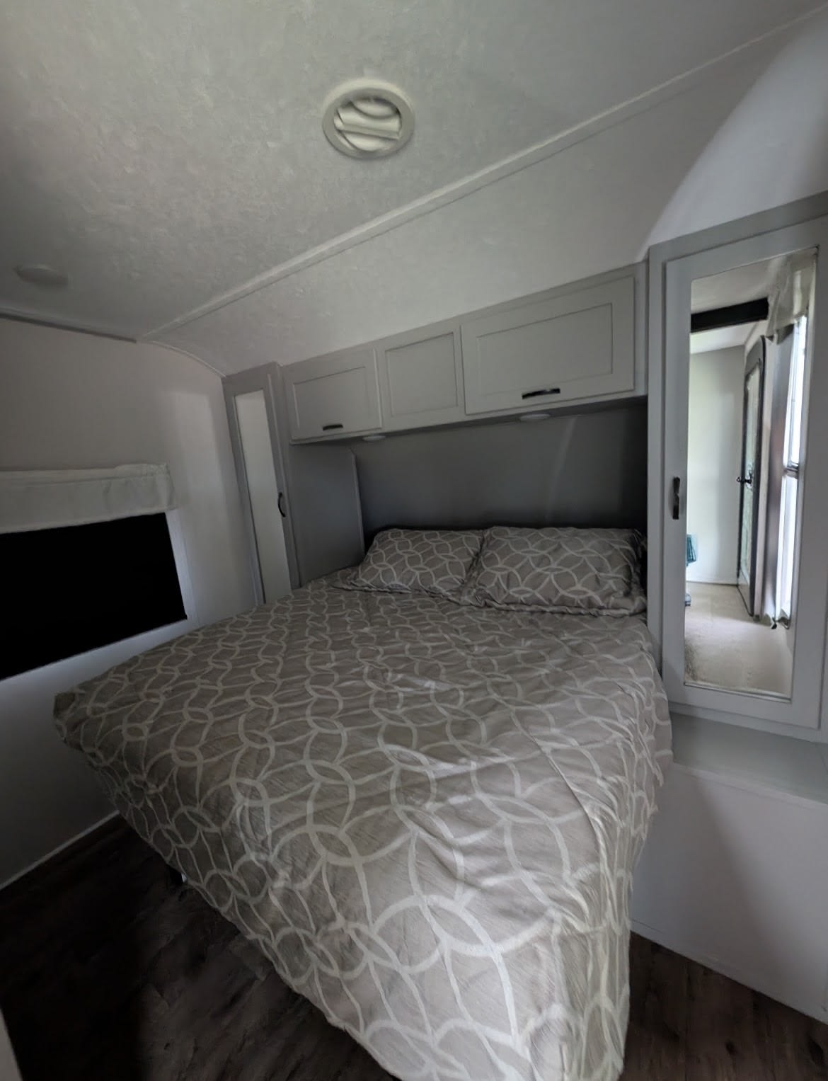 Compact RV rental bedroom with patterned bedding, overhead storage, and a mirrored closet, perfect for travel comfort.. Forest River Vibe 2021