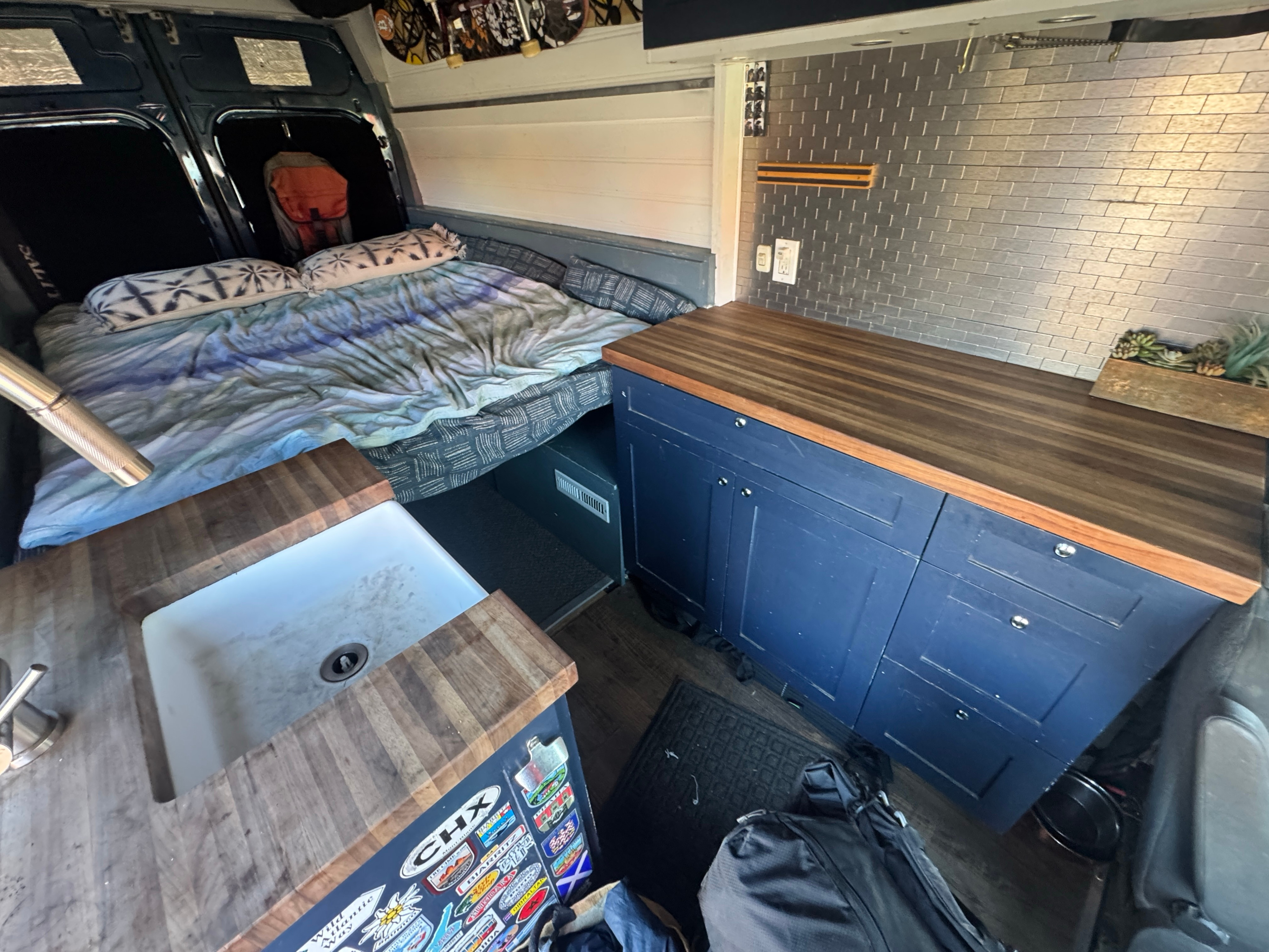 RV rental: Cozy custom van interior featuring a wooden countertop kitchen with sink, blue cabinets, and a comfortable rear bed.. Ford Transit 2019