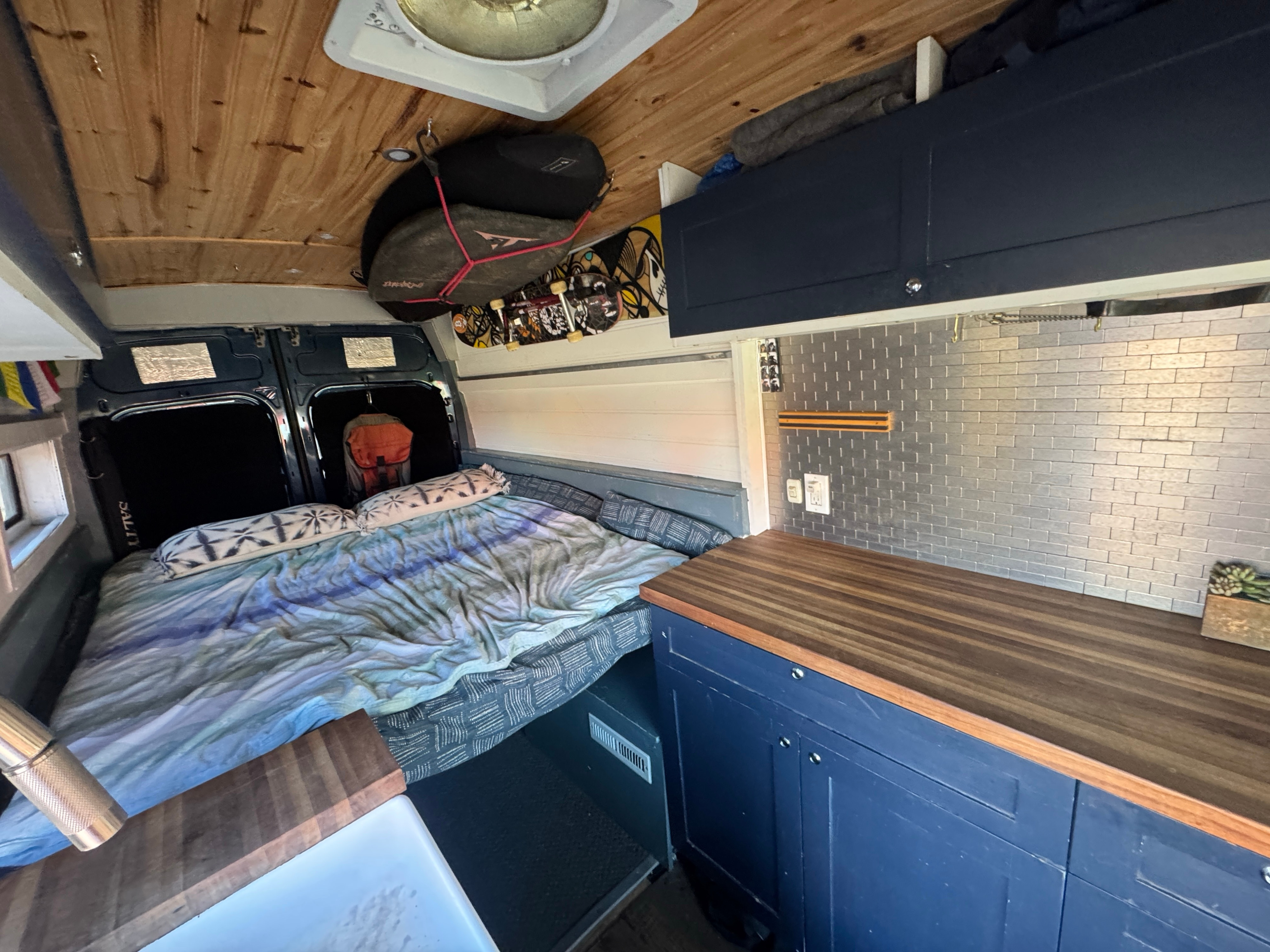 Cozy van conversion interior for your next RV rental adventure. Features a bed, kitchen counter, and storage.. Ford Transit 2019