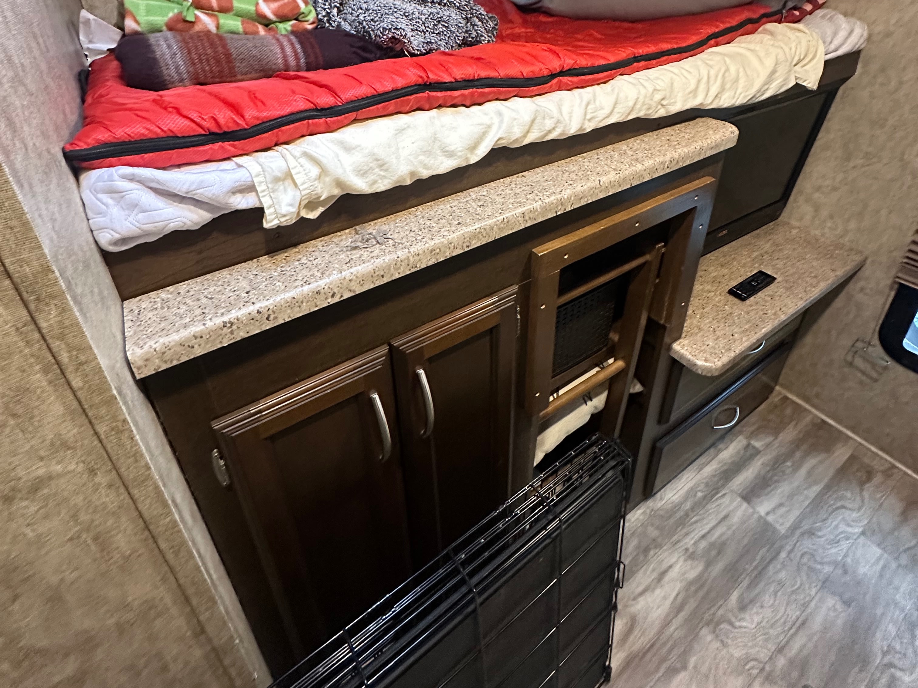 RV rental interior showing a cozy bunk bed with a red sleeping bag, wood cabinets, countertops, and a folded pet crate.. Crusader Crusader Fifth Wheel 2018