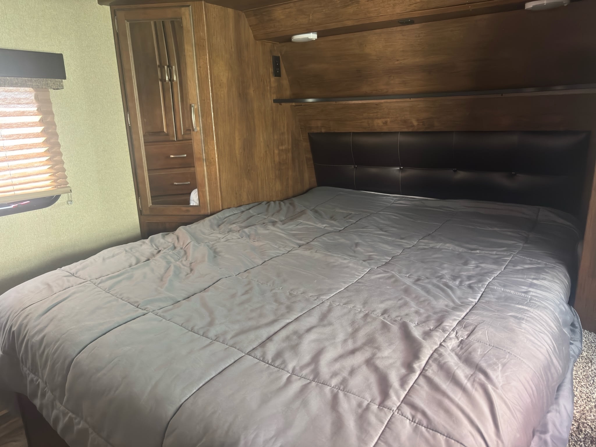 Comfortable RV rental bedroom featuring a large bed with a gray comforter, black headboard, and wood cabinetry.. Grand Design Reflection 2019