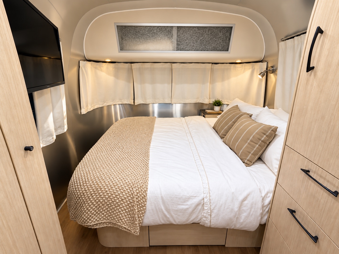 Cozy RV rental bedroom with comfortable bed, modern wood cabinets, and TV, perfect for your next trip.. Airstream International 2017