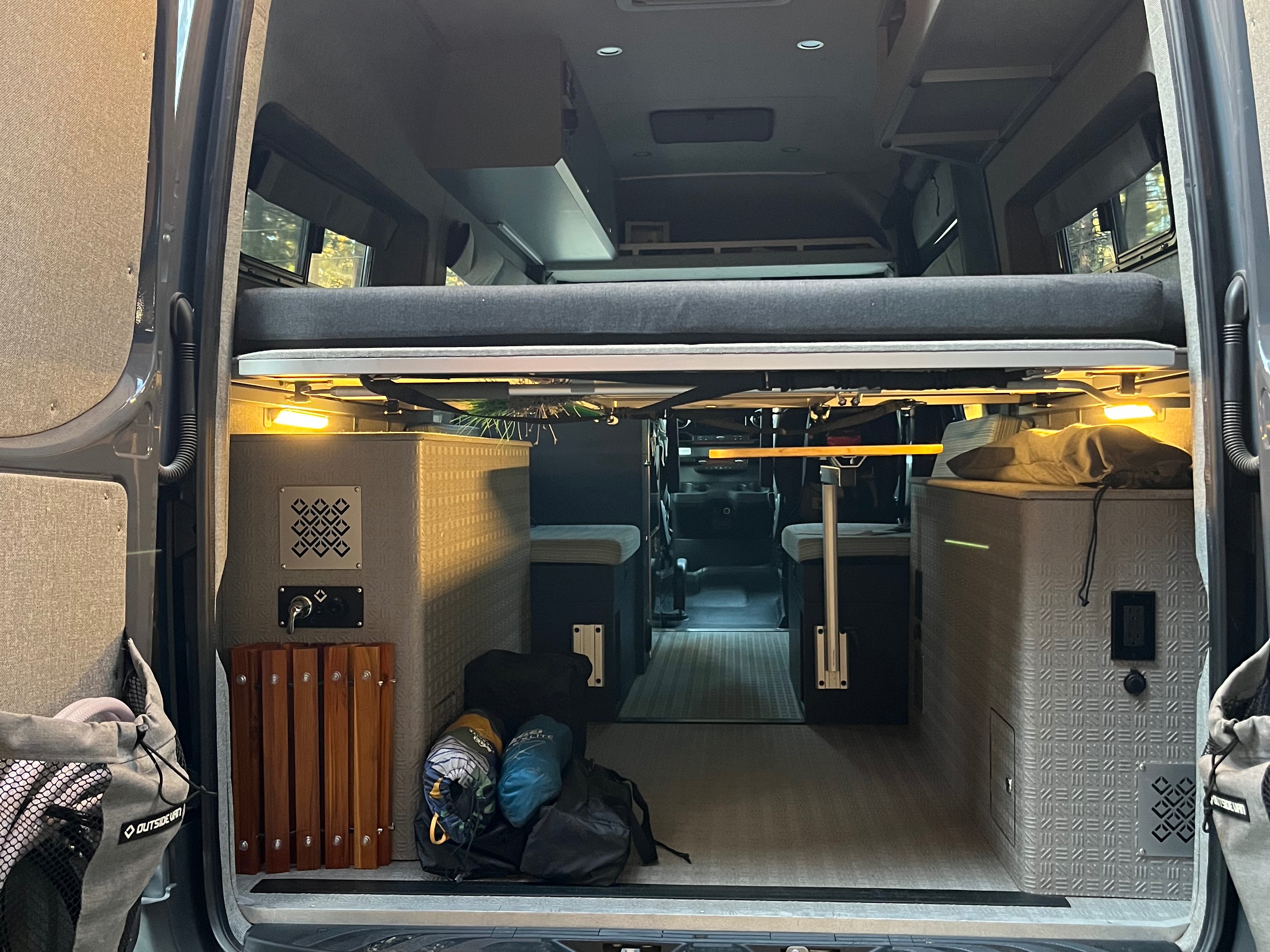 Rear view of an rv rental camper van, revealing a raised bed, under-bed storage, seating, and lighting for travel comfort.. Mercedes Benz Sprinter 144 High Roof 4WD 2020