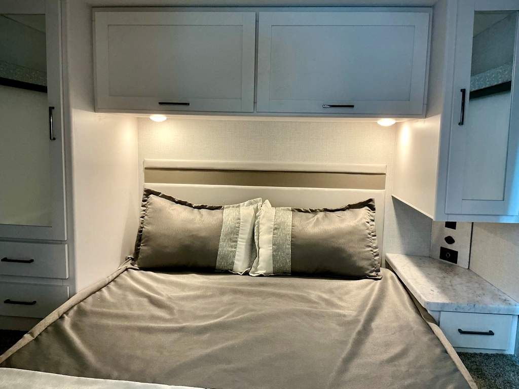 Inside a modern RV rental bedroom featuring a comfy bed, storage cabinets, and a bedside shelf with outlets.. Four Winds 28Z 2026