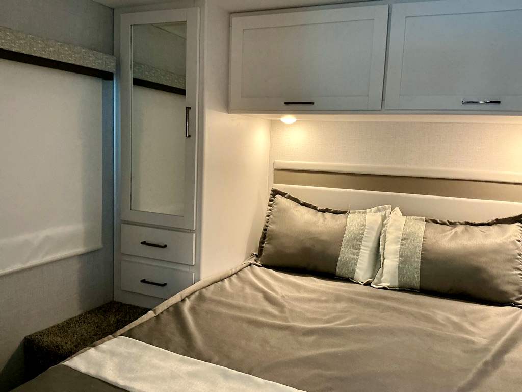 Cozy RV rental bedroom featuring soft bedding, overhead cabinets, and a mirrored wardrobe for comfortable travel.. Four Winds 28Z 2026