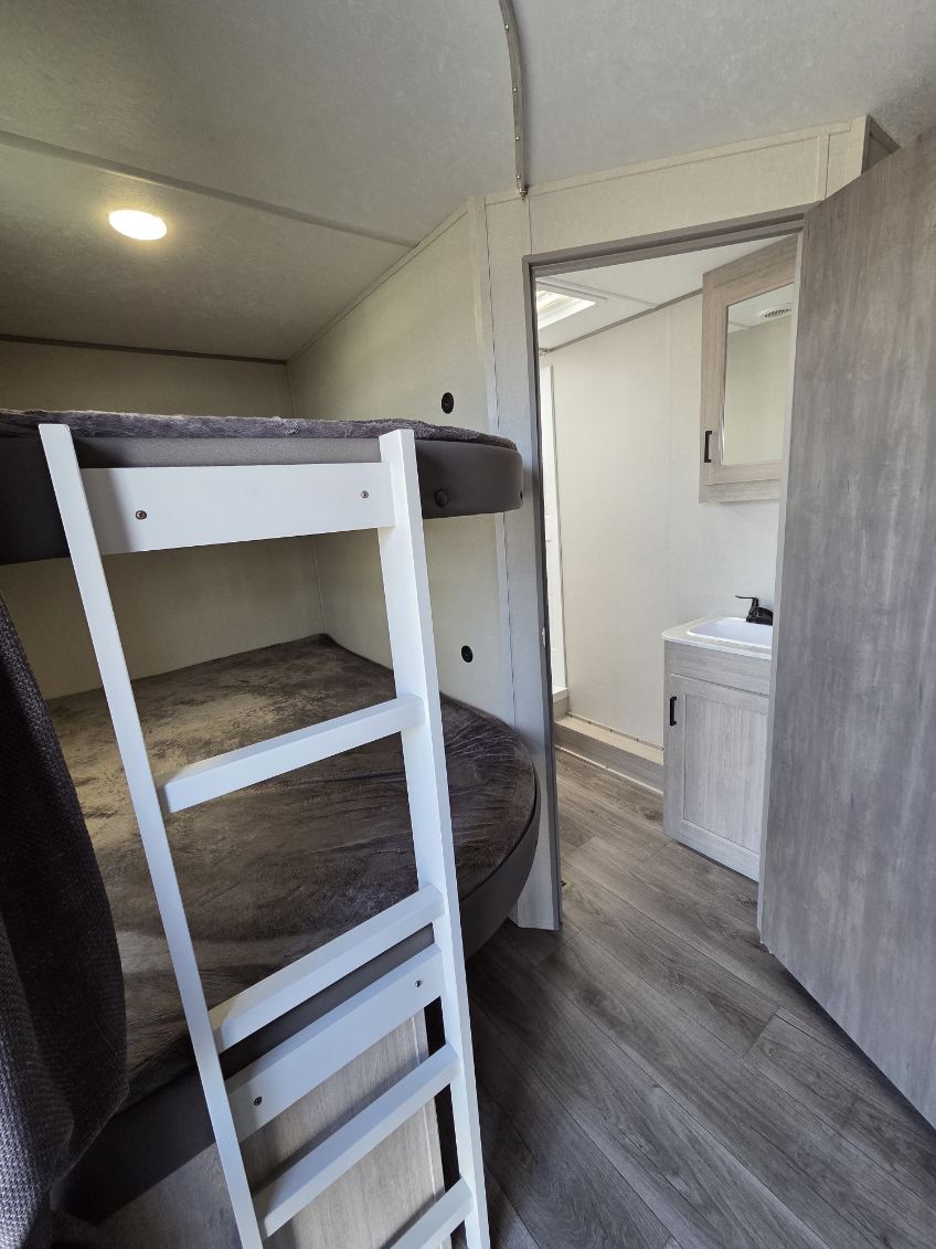 RV rental featuring cozy bunk beds with a white ladder and an adjoining compact bathroom with a sink, vanity, and mirror.. Catalina 263BHSCK 2025