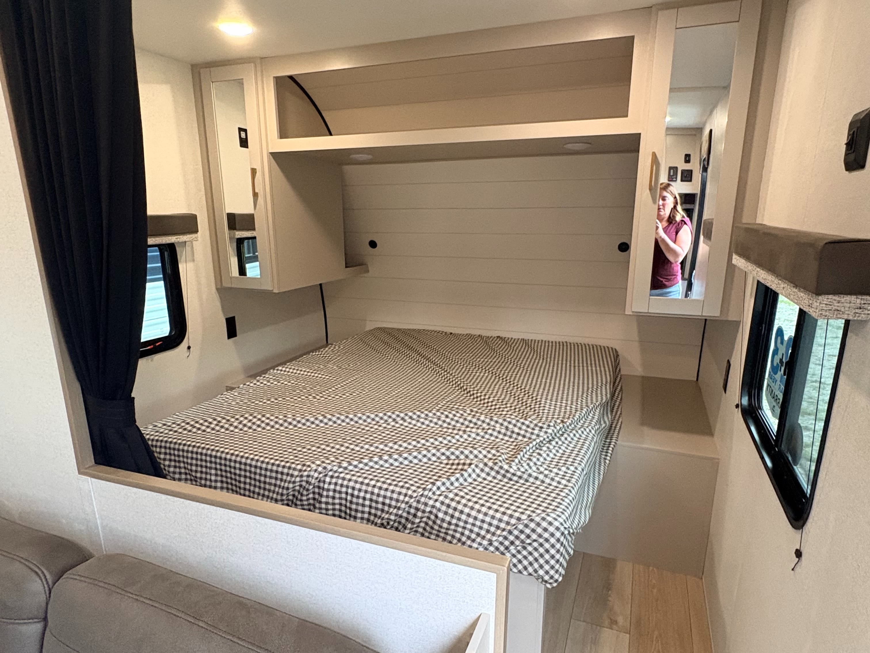 This RV rental features a comfortable bedroom with a checkered bed, built-in storage, and side windows.. Jayco Jay Flight 2027