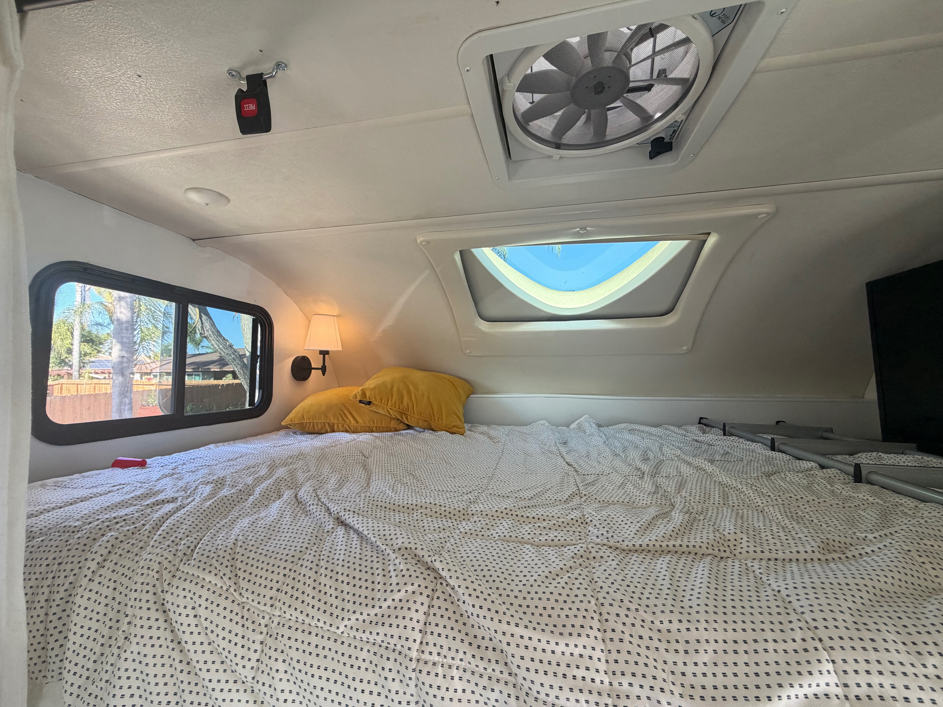 This RV rental's bedroom features a patterned bed, yellow pillows, window view, ceiling fan, skylight, and wall lamp.. Thor Quantum 2018