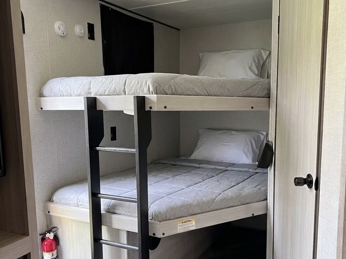 This RV rental features cozy bunk beds with a ladder, perfect for family adventures. Safety features like a fire extinguisher are visible.. Crossroads RV Zinger 2024