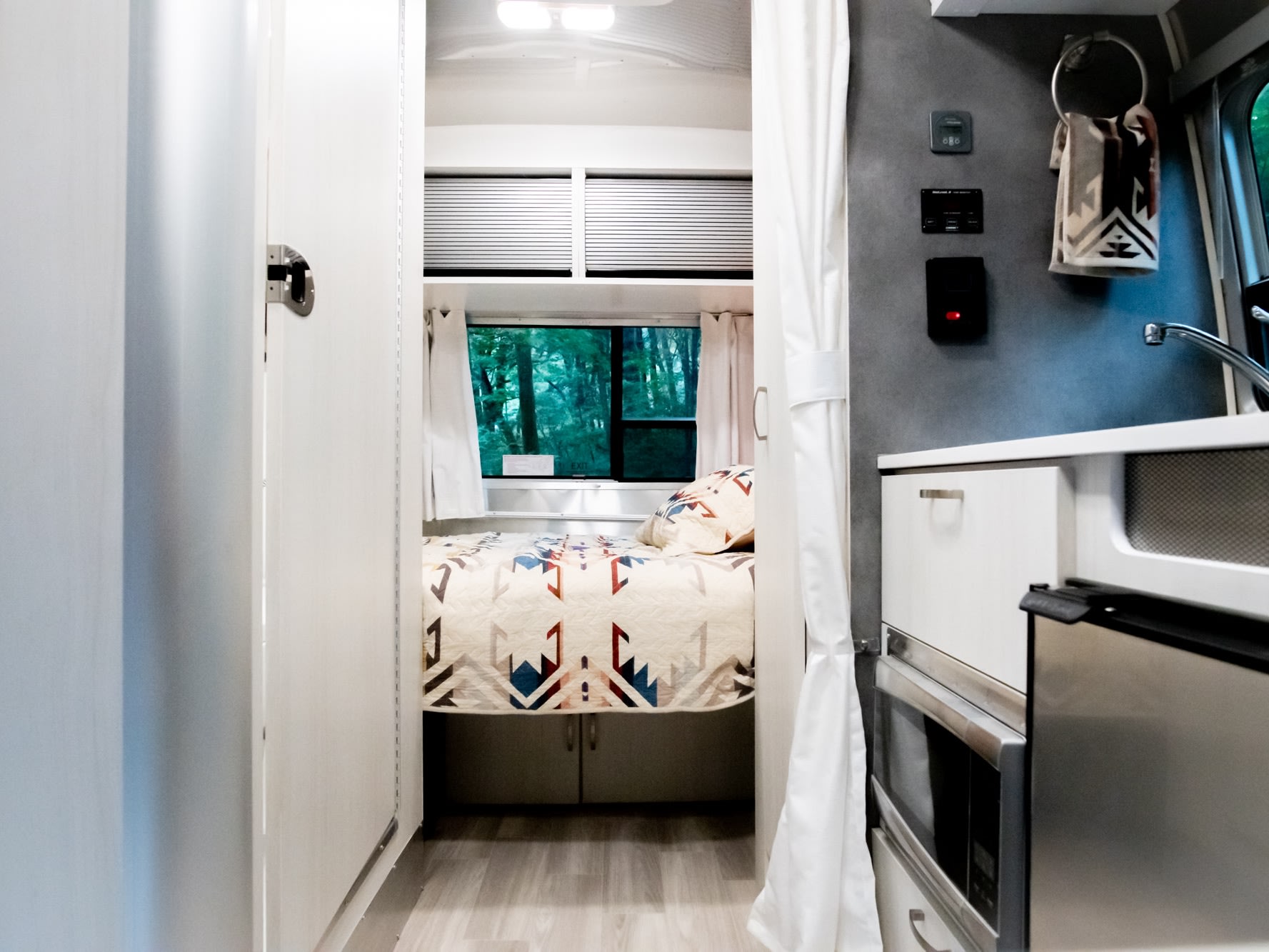 Bright & modern RV rental interior with a cozy bedroom, compact kitchen, & nature views. Ideal for travel!. Airstream Bambi 2022