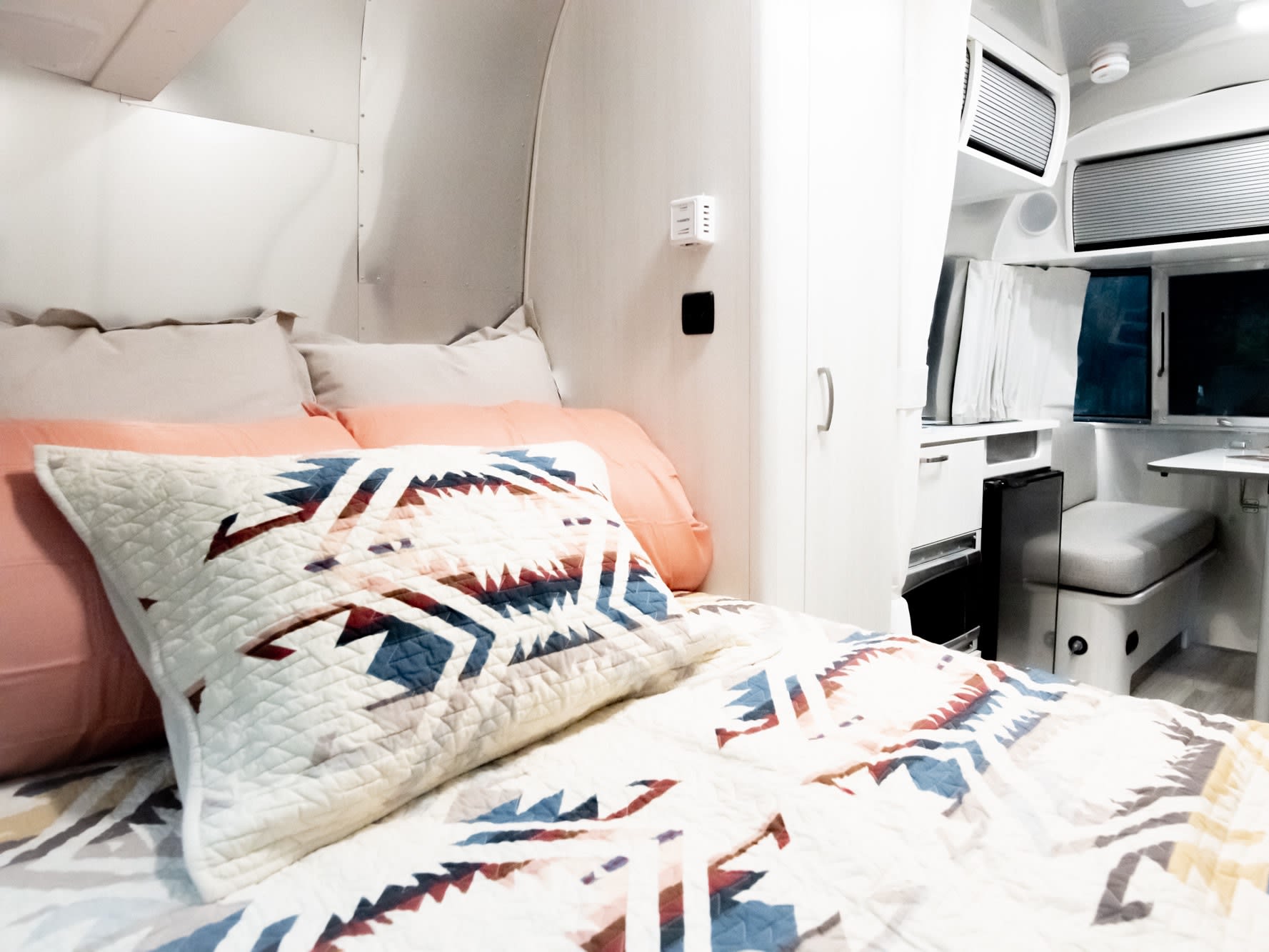 Modern RV rental interior showcasing a cozy bedroom with patterned bedding and a compact dining area.. Airstream Bambi 2022