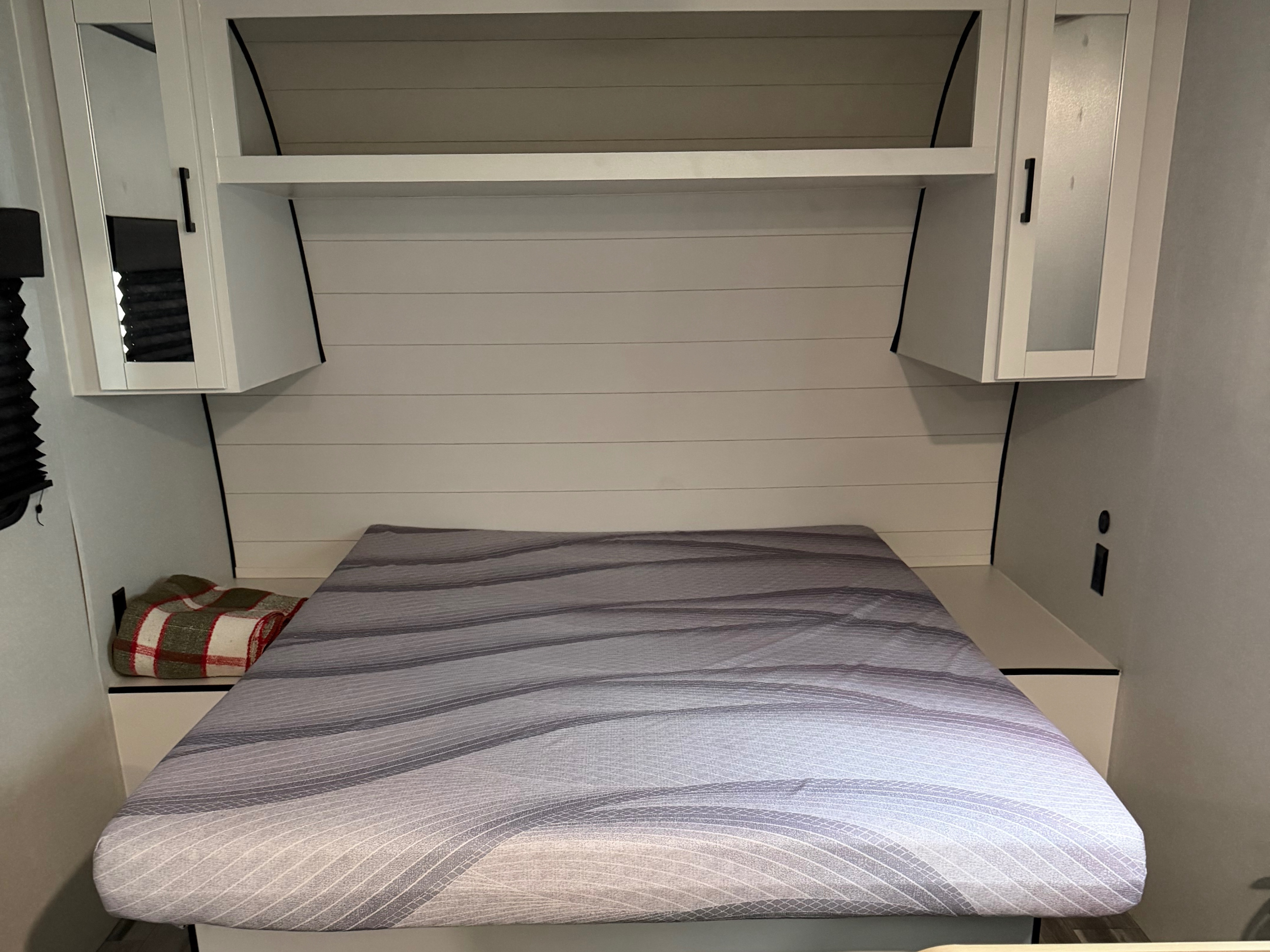 RV rental bedroom with a striped bed, overhead cabinets, shiplap wall, and blanket, offering compact comfort.. Jayco Jay Flight SLX Sport Edition 2026