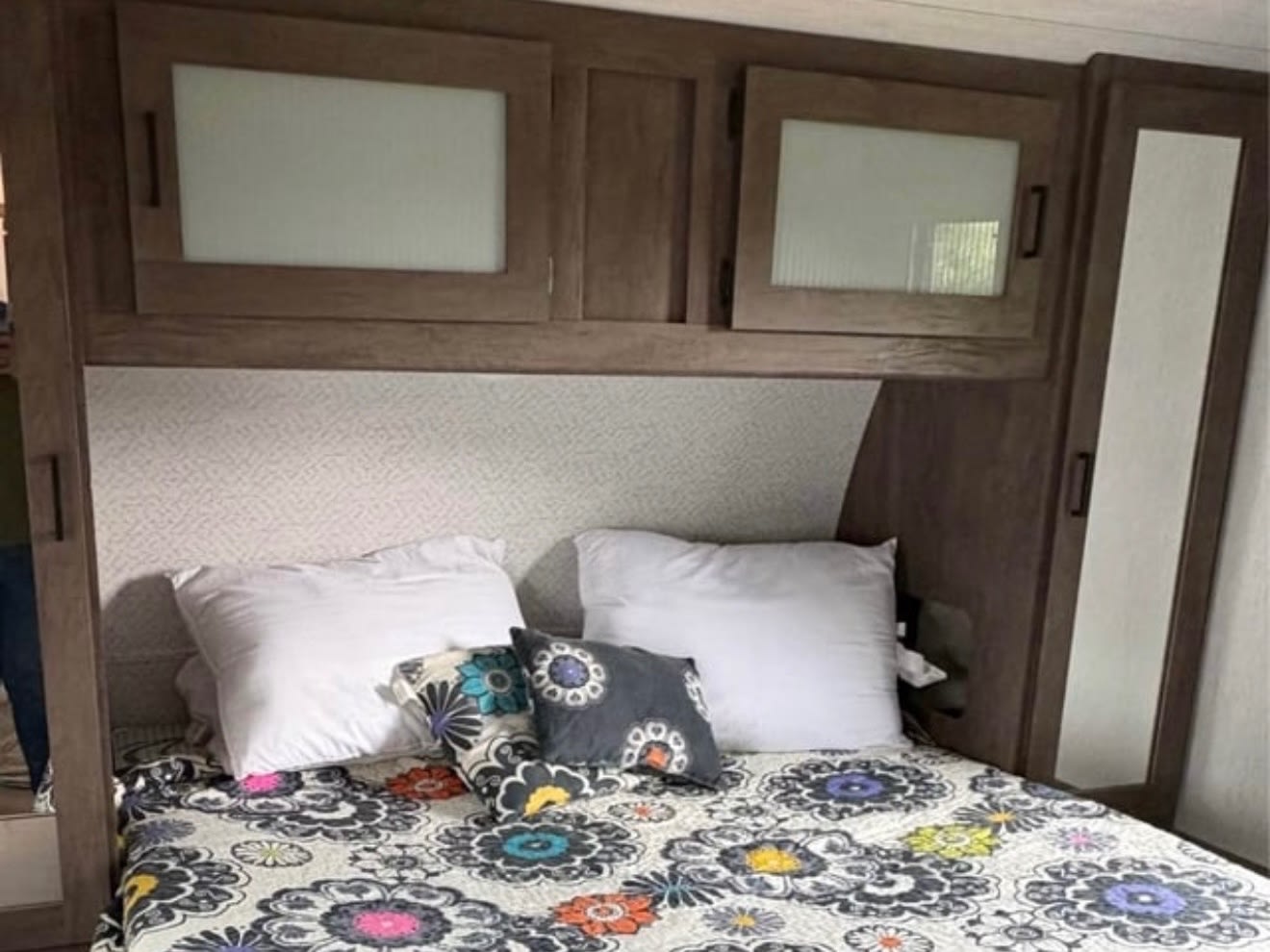 Cozy RV rental bedroom with a floral bedspread, white pillows, and practical wood-toned overhead storage cabinets.. Forest River Salem 2022