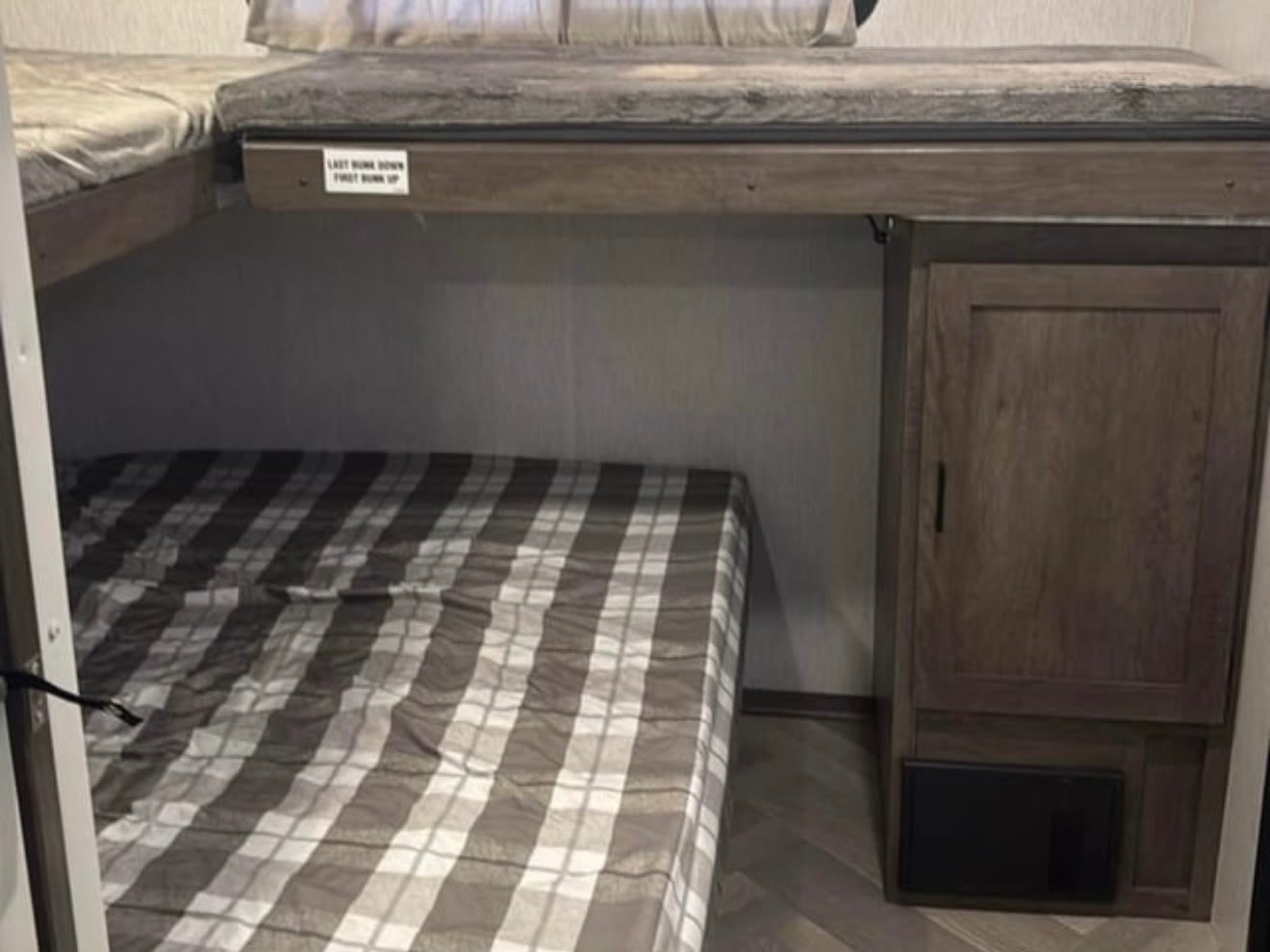 RV rental bunk beds. Lower bed with plaid comforter, upper bunk above, and a dark wood storage cabinet on the right.. Forest River Salem 2022