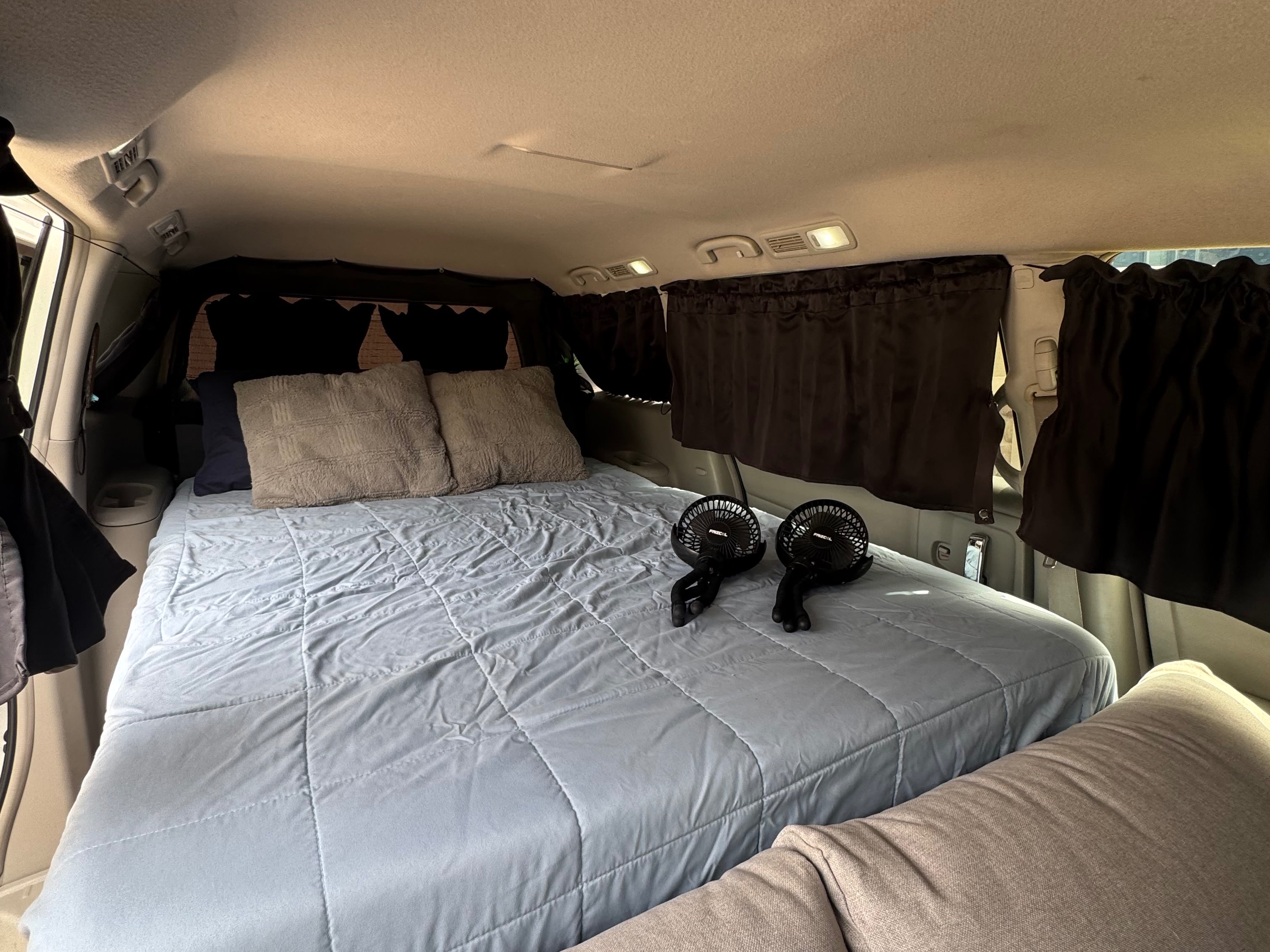 Inside a comfortable RV rental with a large bed, fluffy pillows, and personal fans, ideal for a road trip or van life.. Nissan Quest 2017