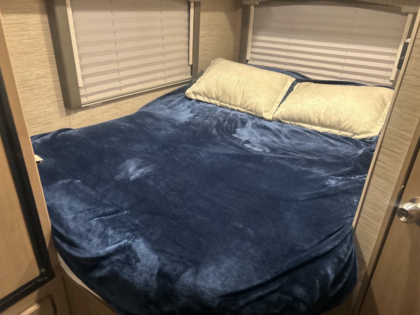This RV rental offers a compact, inviting bed with a soft blue blanket and two light pillows, ready for a restful journey.. Thor Chateau 2022