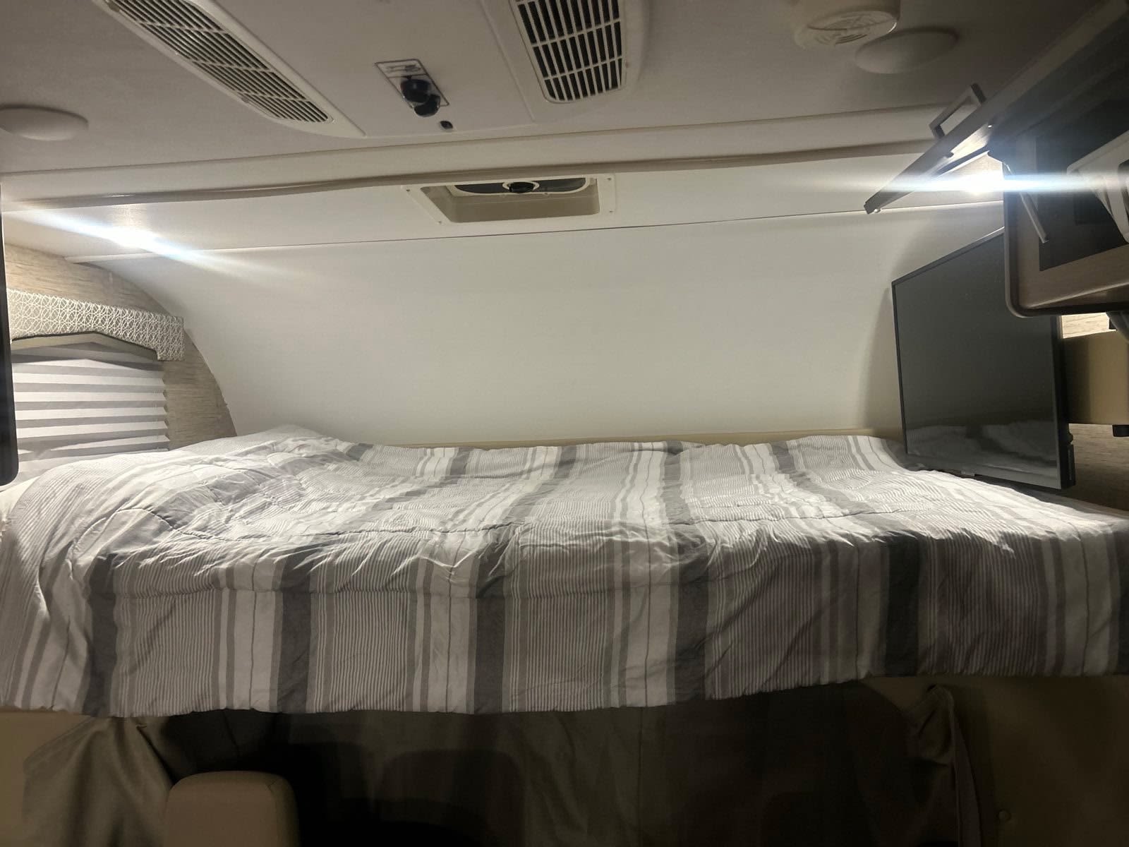Cozy RV rental cab-over sleeping area with a striped bed, overhead AC, and TV. Perfect for a comfortable stay.. Thor Chateau 2022