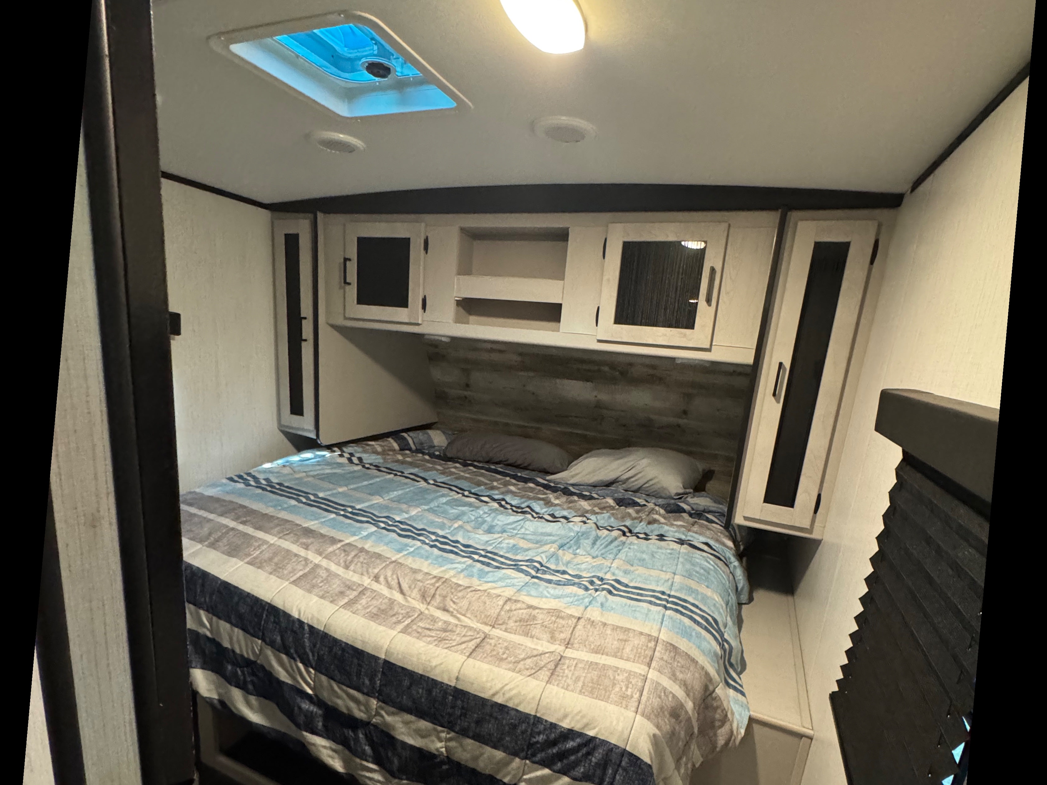 Striped blue, white, and gray bedding in a cozy RV rental bedroom with overhead cabinets and a ceiling vent.. Heartland RVs Mallard 2022